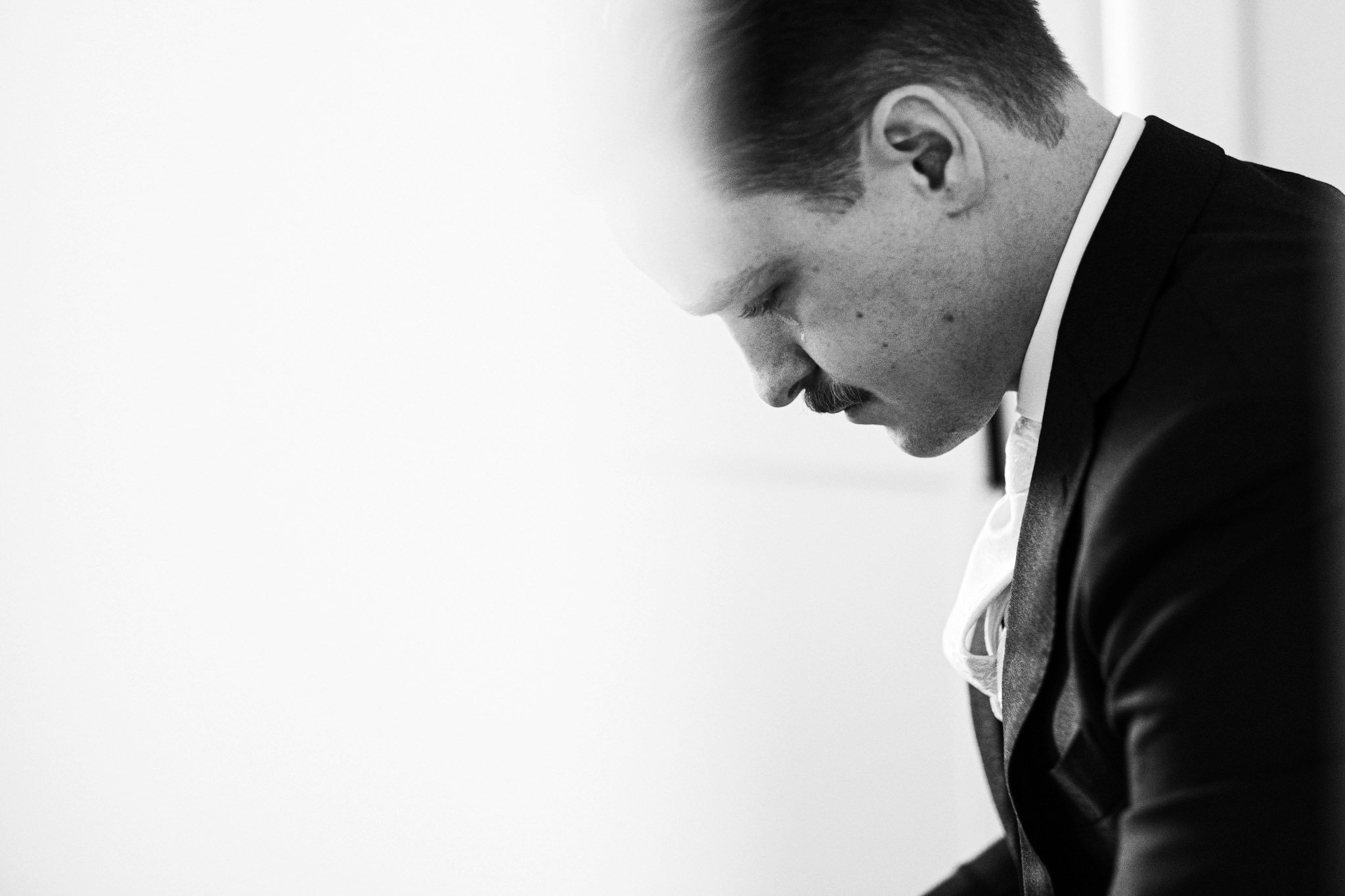 A black and white photo of a man in a suit with a mustache, looking downward in a contemplative pose.