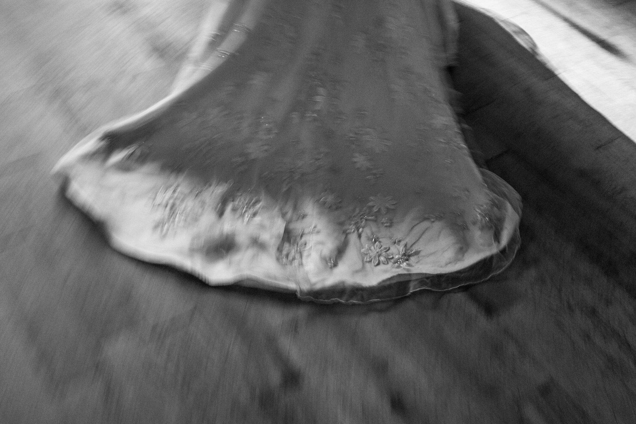 A black and white photo of a floral-patterned tablecloth covering a table or surface, with some motion blur.