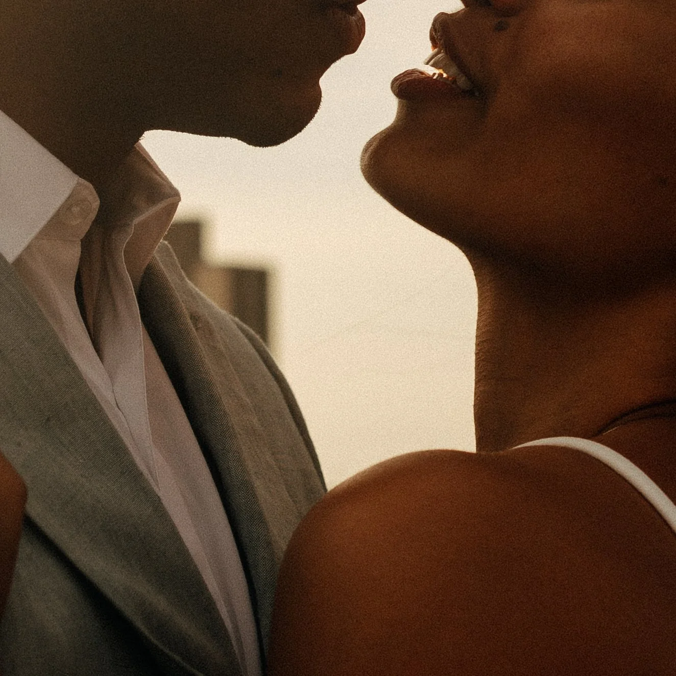 Close-up of a man and woman with their faces close to each other, appearing to be about to kiss, with warm ambient lighting.