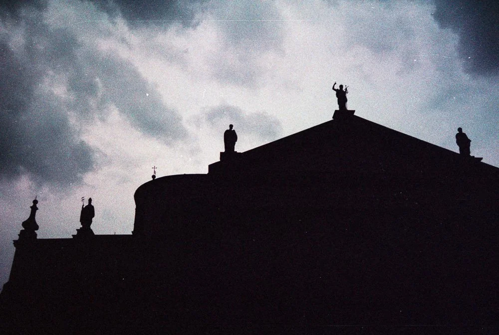 Silhouette di una chiesa con statue sul tetto contro un cielo nuvoloso.