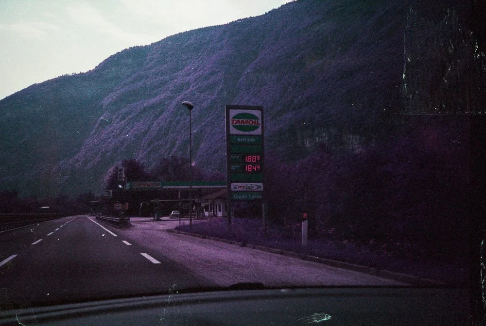 Stazione di servizio su strada, montagne sullo sfondo, insegna con prezzi del carburante Tamoil.