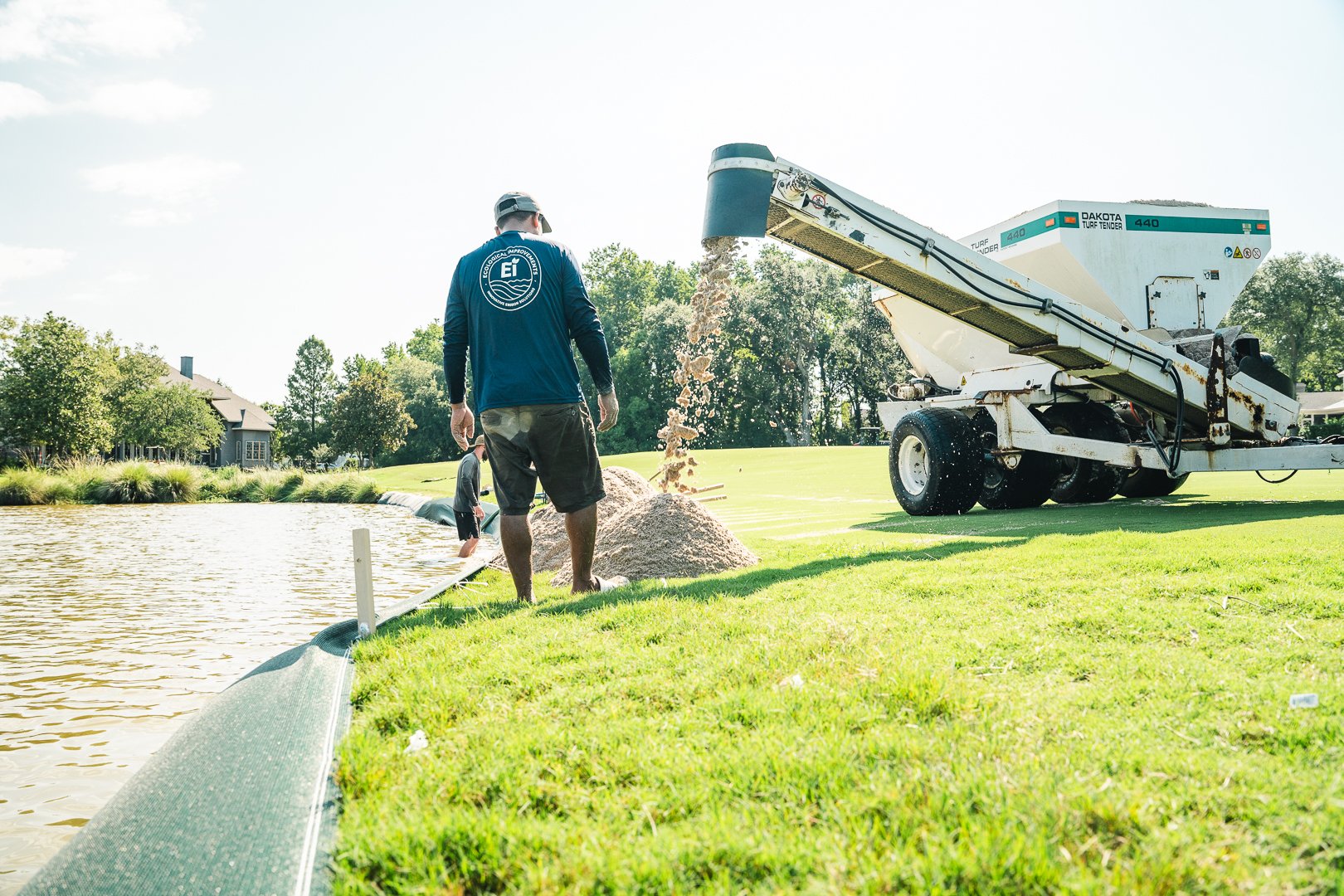 Men installing a pond liner by a pond with a gravel pump nearby on a sunny day.