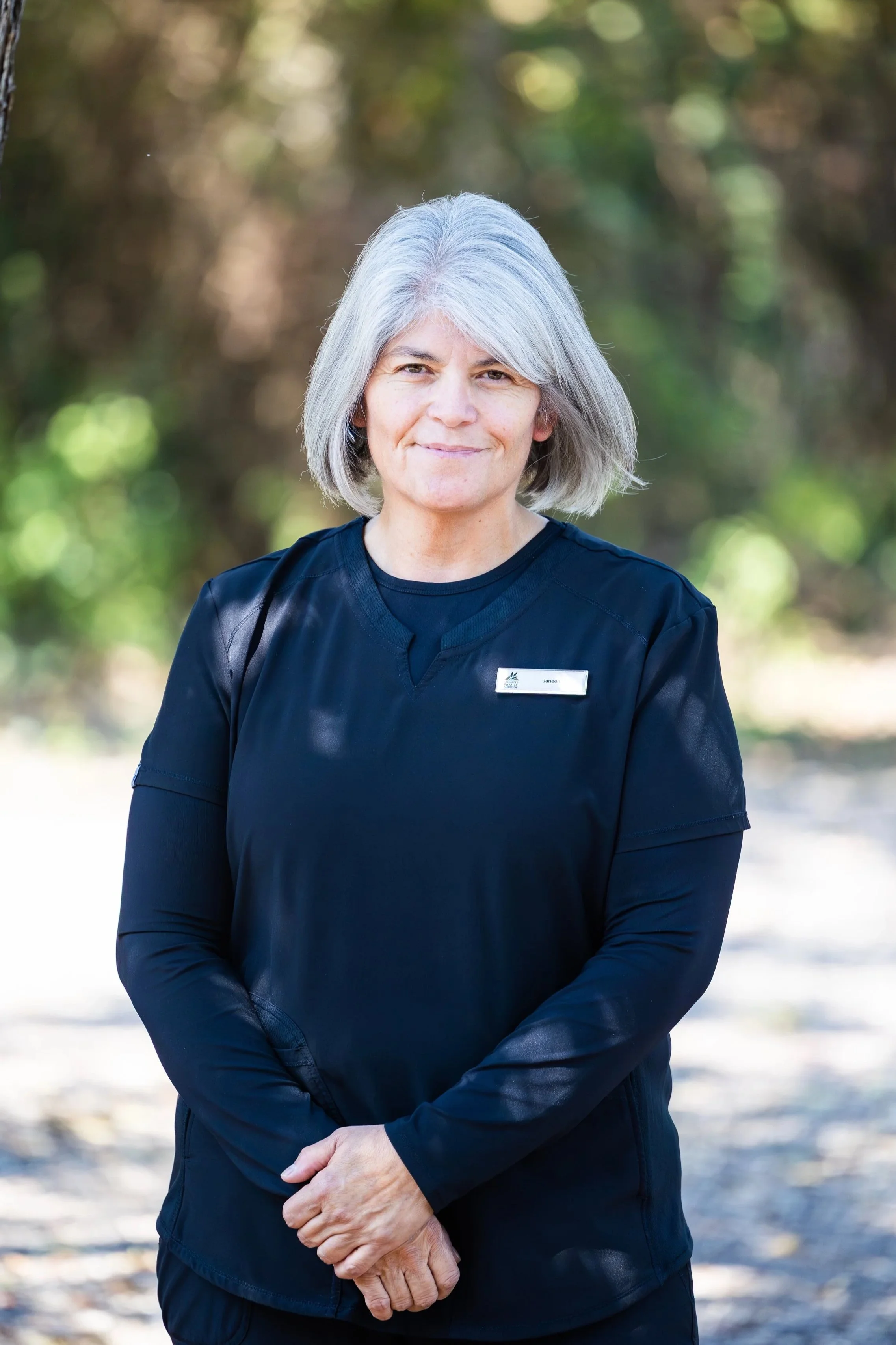 A middle-aged woman with gray hair wearing a black uniform outdoors with a blurred natural background.