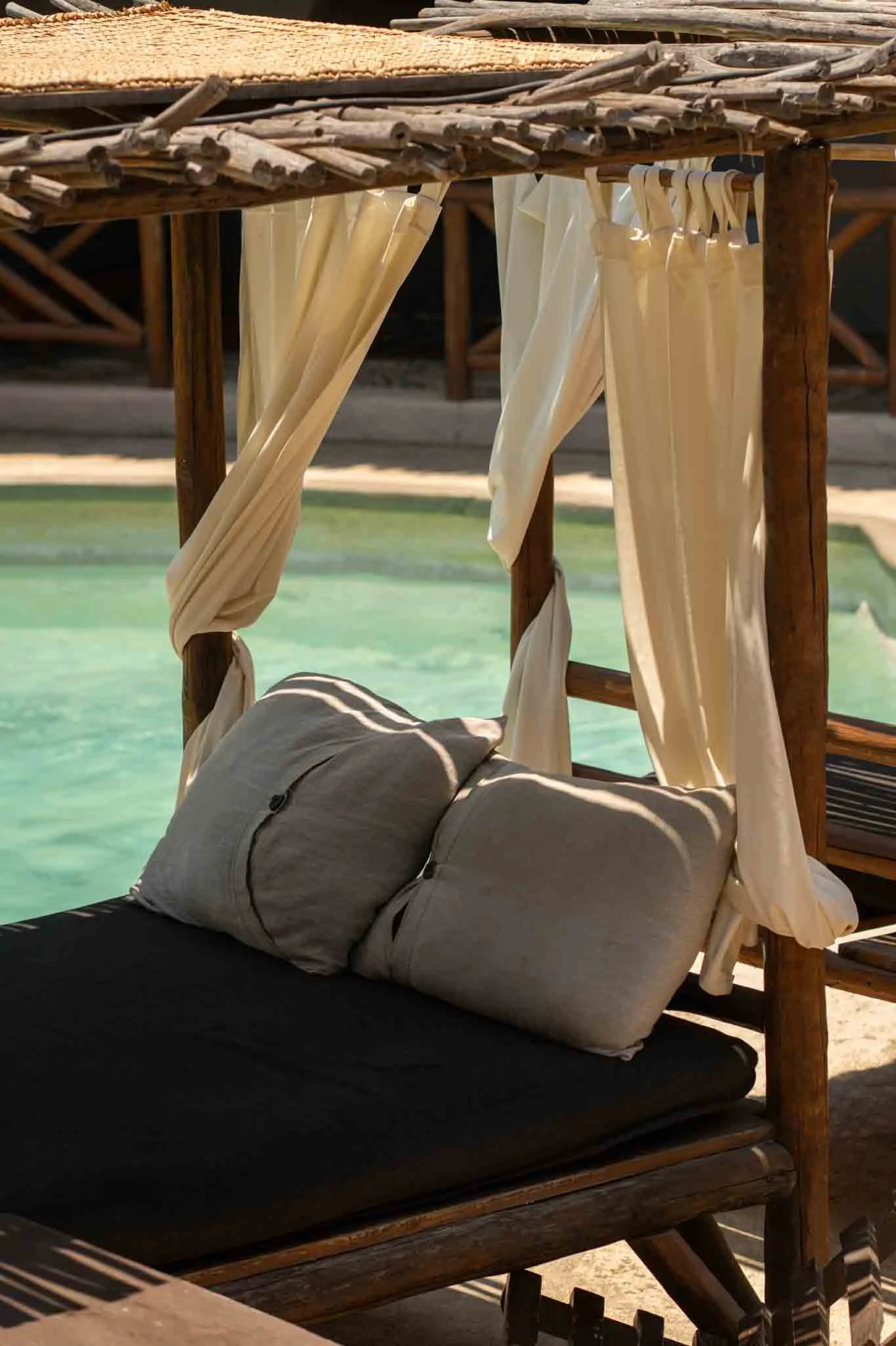 Cabaña de madera con cortinas beige, sofá con cojines, vista a una piscina con agua turquesa. hotel baxar pie de la cuesta 