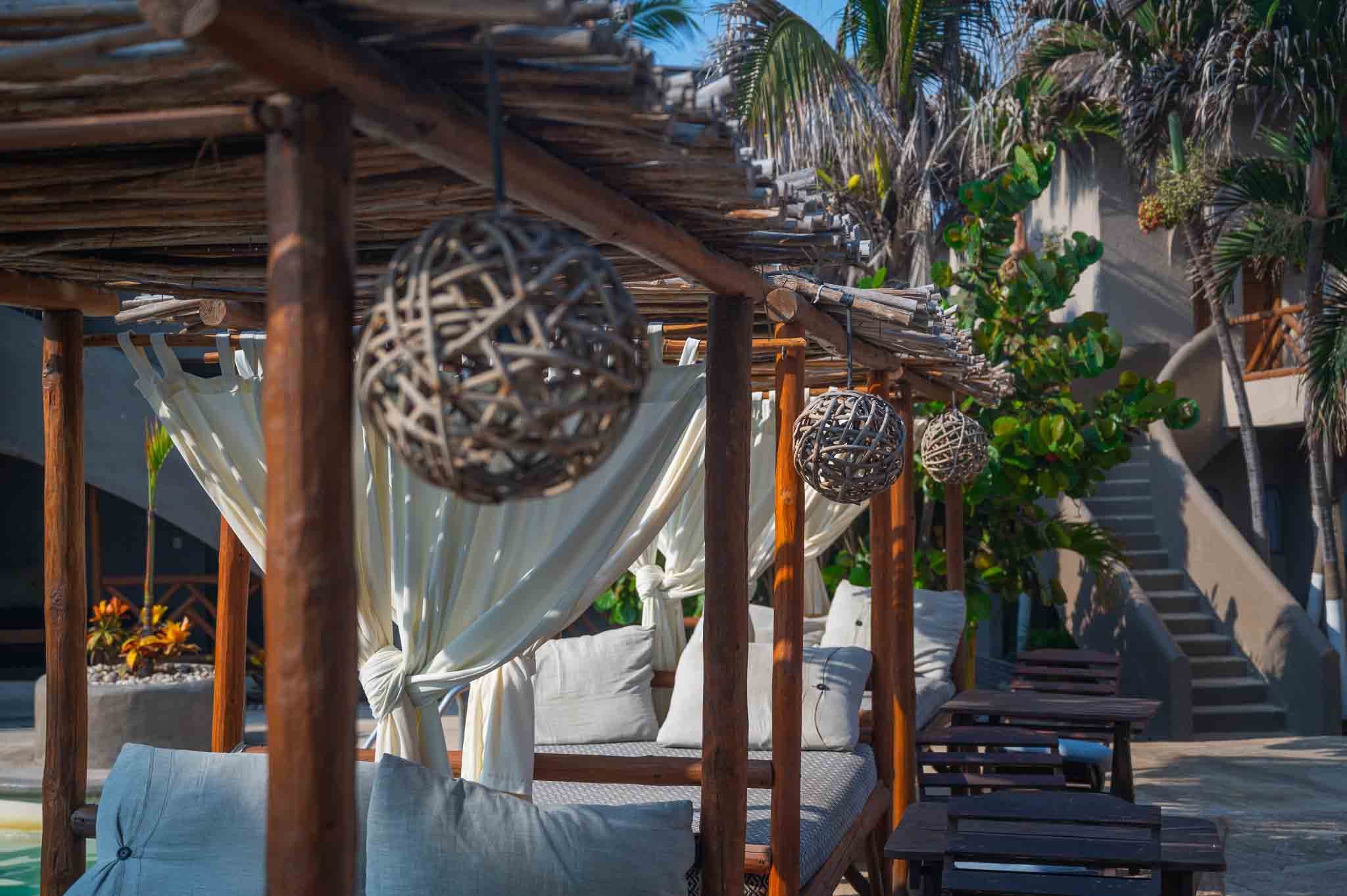 Árboles de madera con cortinas blancas y faroles decorativos en un espacio exterior con muebles de terraza y plantas tropicales. hotel baxar pie de la cuesta 