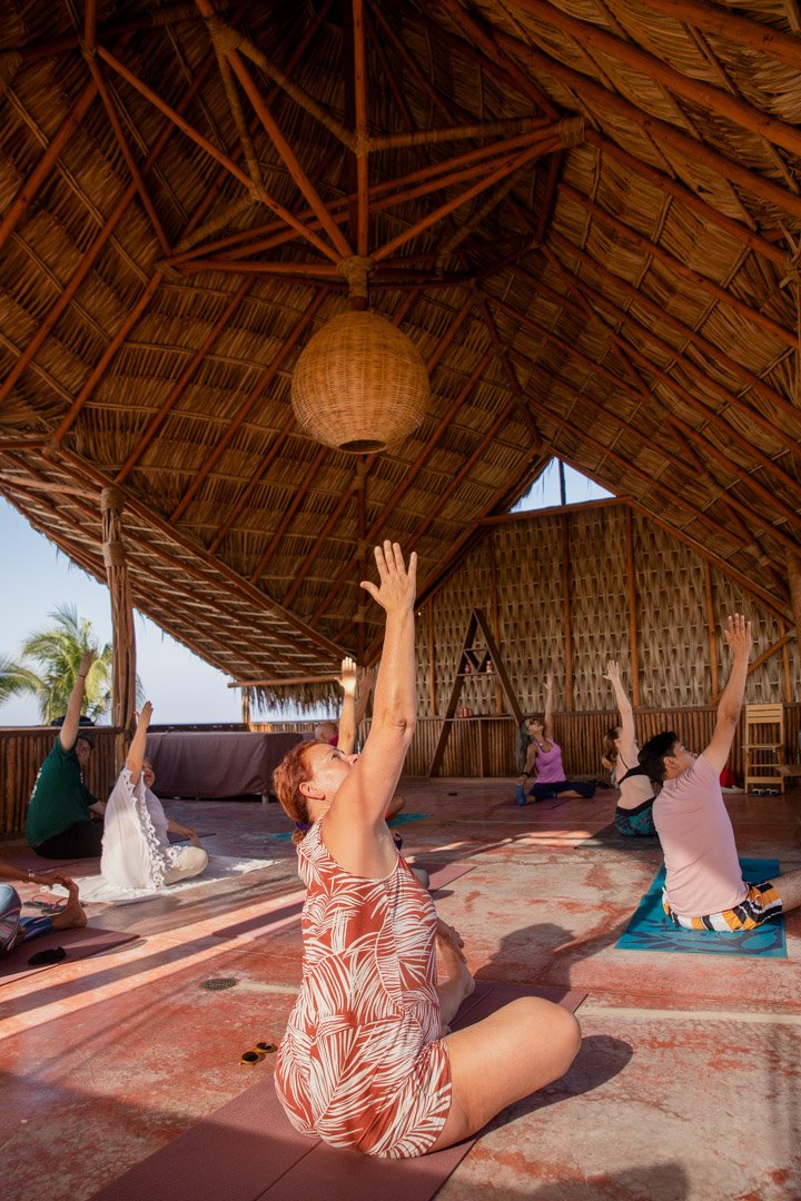 Grupo de personas practicando yoga en una baxar hotel, palapa shala al aire libre, levantando los brazos en una posición de estiramiento de yoga