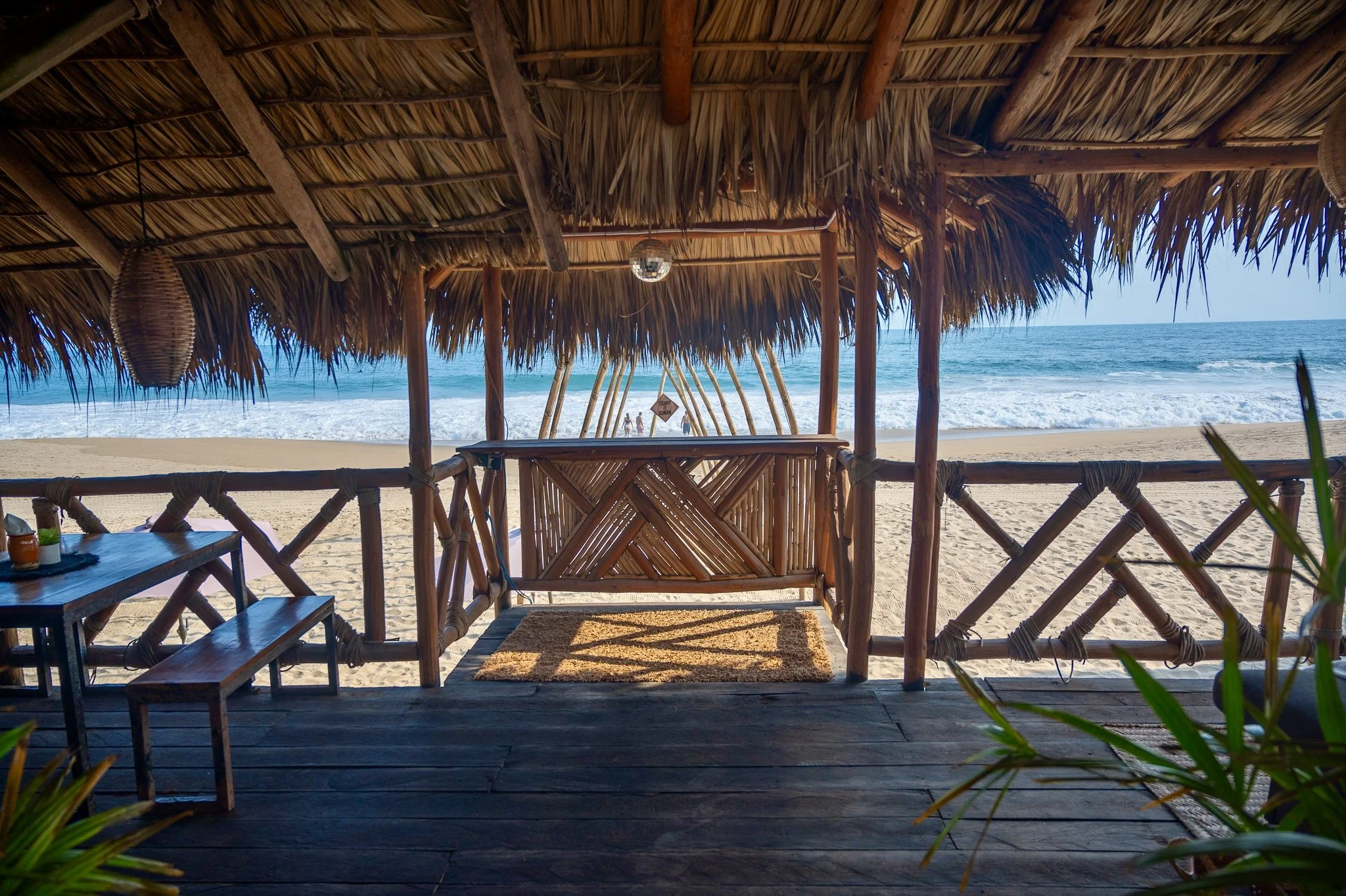 Palapa de madera y paja en la playa con vista al mar y personas en la arena.  club de playa pie de la cuesta, hotel boutique baXar acapulco