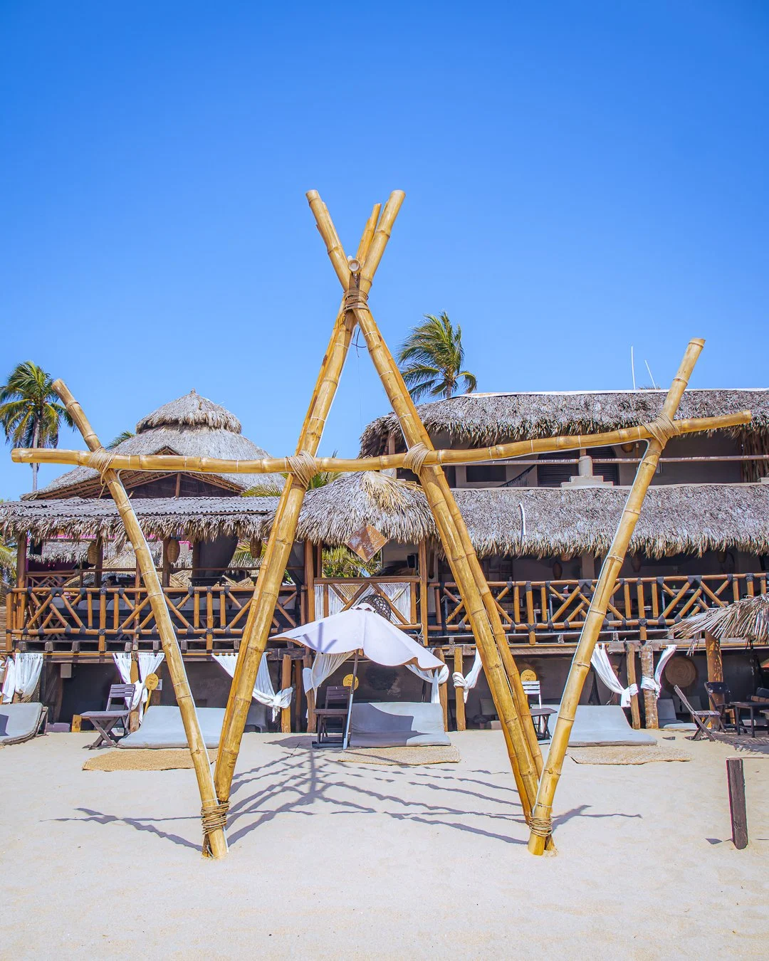 Estructura para columpios en la playa con cabañas de palma y sombrillas. Playa Pie de la Cuesta, Acapulco, Hotel baXar