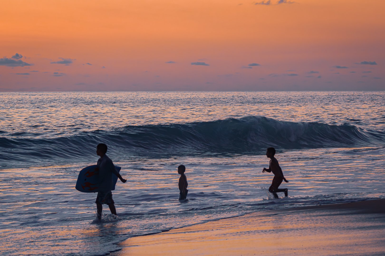 Niños jugando en la playa al atardecer, con olas y cielo con tonos anaranjados y rosados.  Hotel boutique baXar playa Pie de la cuesta Acapulco