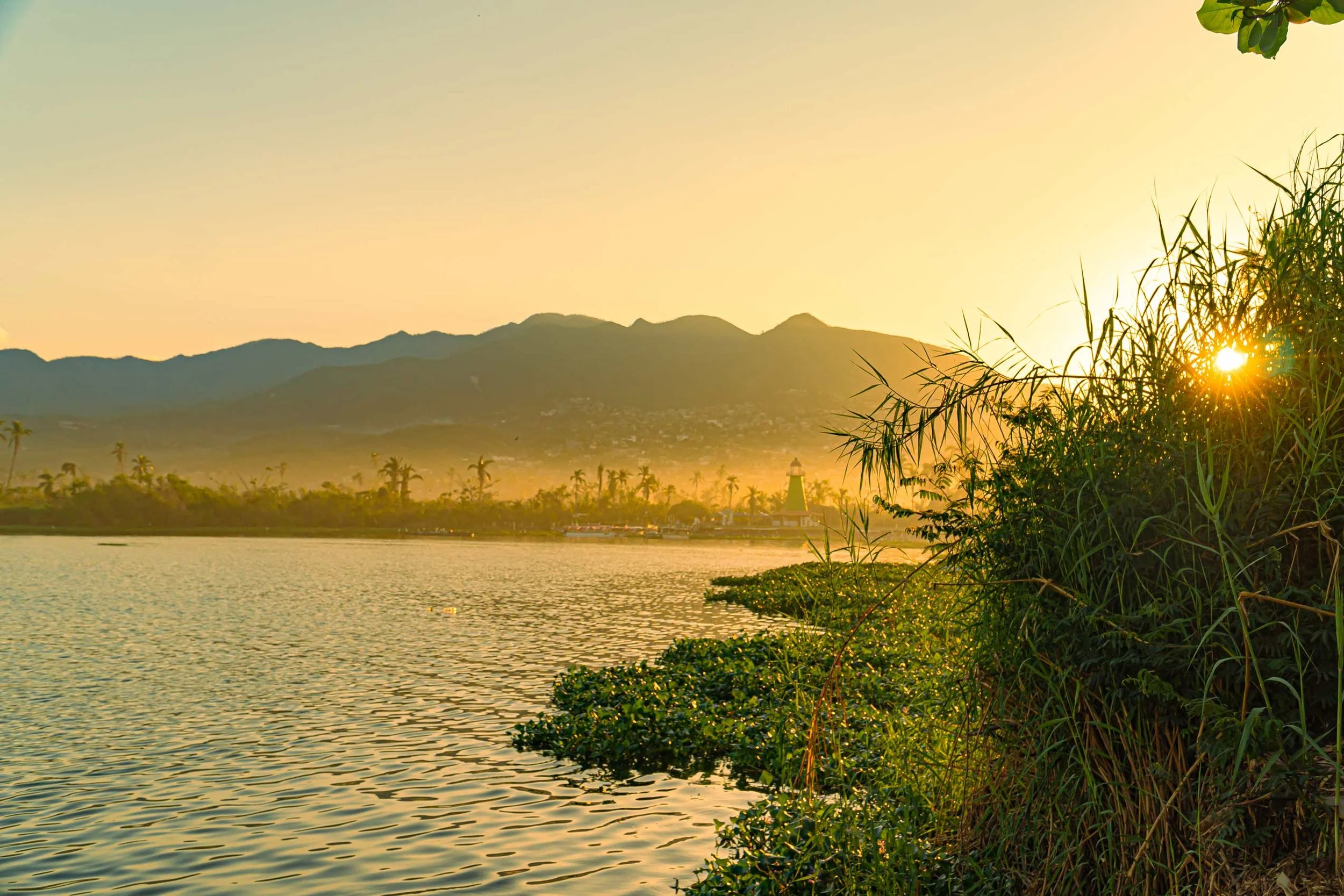 Atardecer sobre laguna coyuca con montañas al fondo y vegetación en primer plano. baxar hotel wellness acapulco