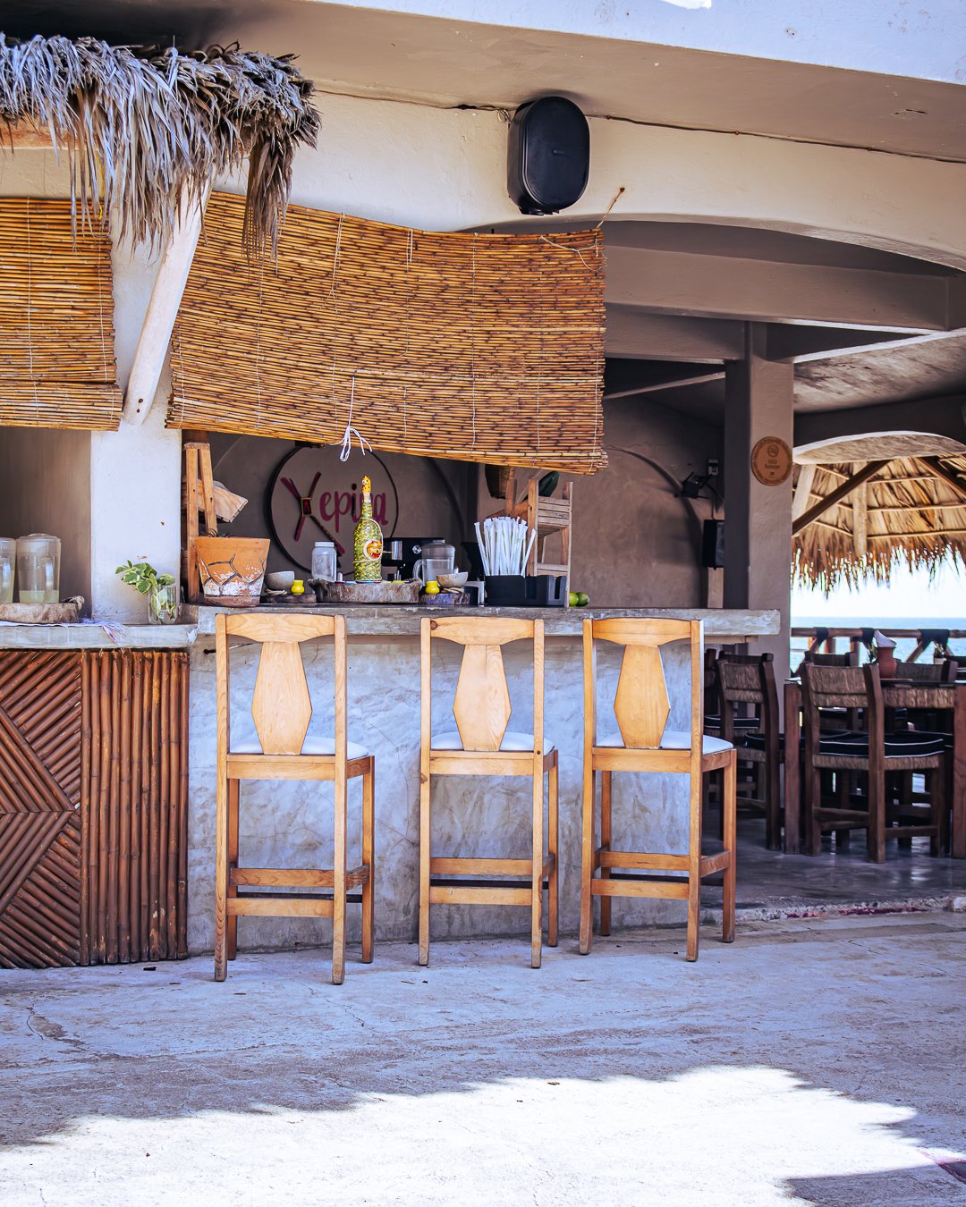 Bar de palapa con sillas de madera en un lugar de ambiente tropical y playa, con decoración rústica y vista al mar.  club de playa pie de la cuesta, hotel boutique baXar acapulco