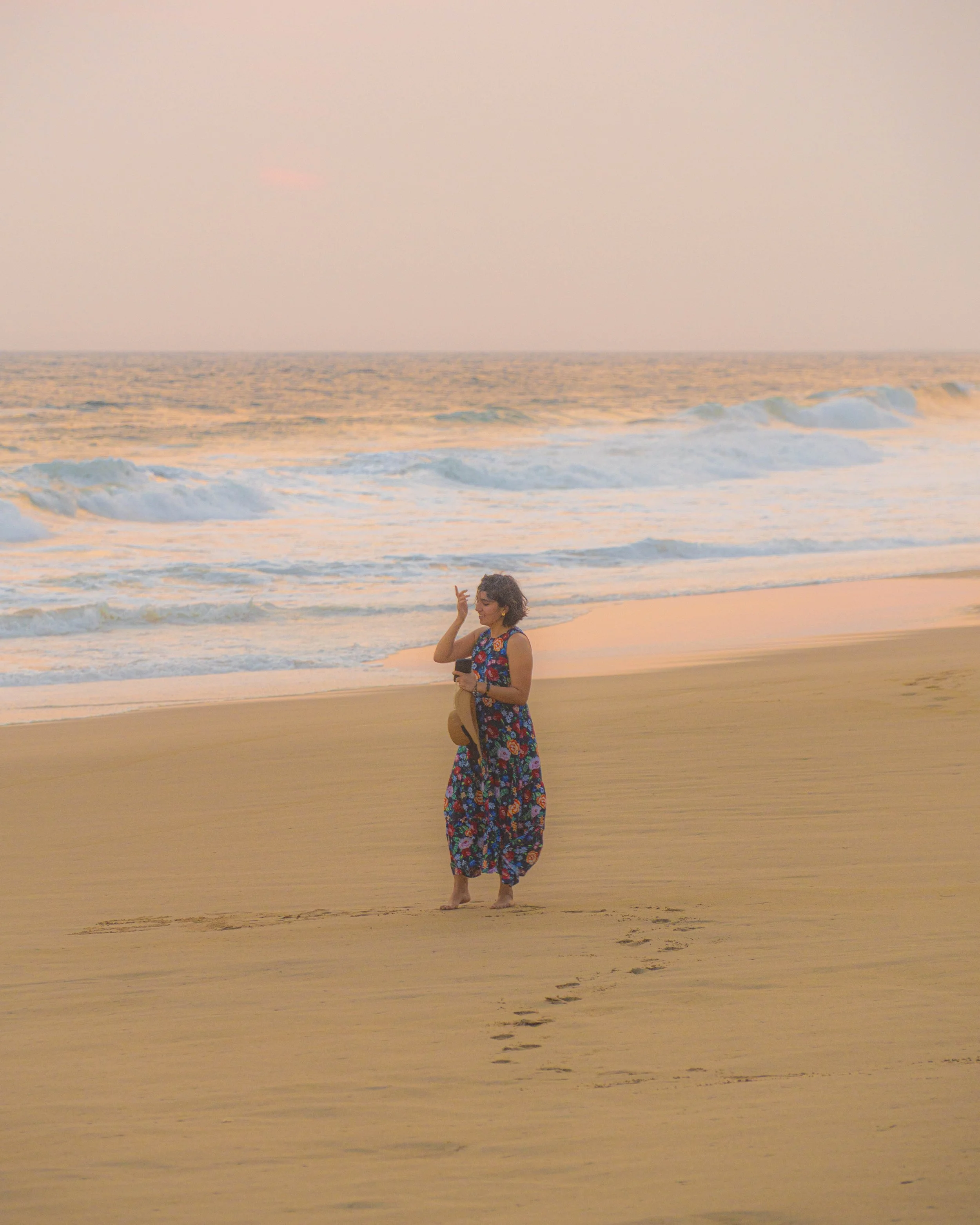 Mujer caminando en la playa durante la puesta del sol, con olas suaves en el fondo y el cielo iluminado por tonos cálidos. playa pie de la cuesta, acapulco, mexico
