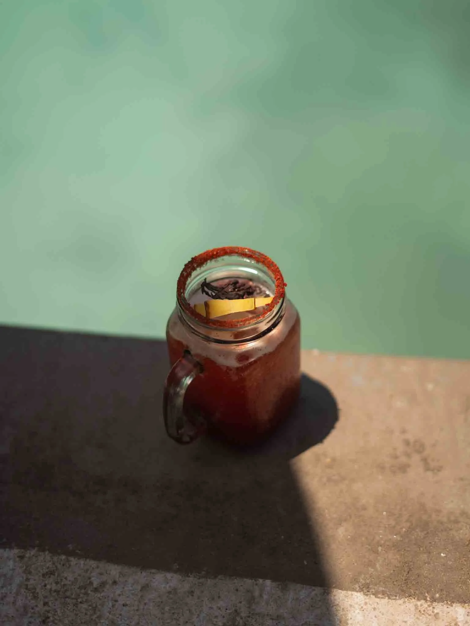 Un vaso de vidrio con bebida y un rodaja de limón en el borde, colocado sobre una superficie de concreto. Fondo de color verde claro. hotel baxar pie de la cuesta 