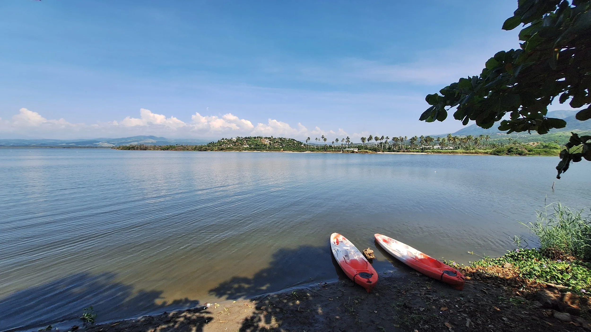 Tres tablas de paddleboard en la orilla de un lago, con árboles y colinas en el fondo bajo un cielo despejado. Hotel baXar pie de la cuesta puesta de sol playa pie de la cuesta