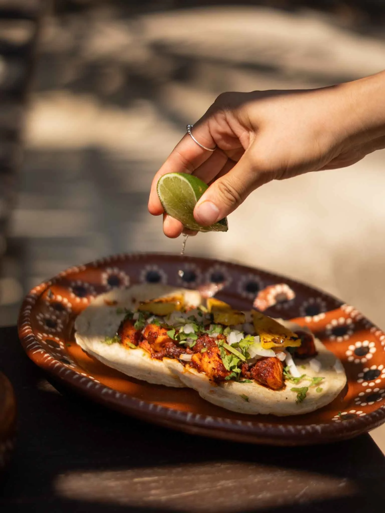 Una mano exprimiendo jugo de lima sobre un taco de carne con verduras en un plato de barro decorado con puntos blancos. restaurante frente al mar hotel baxar club de playa pie de la cuesta