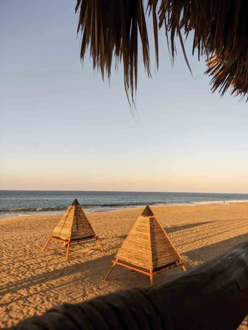 Playas con sombrillas de madera en la arena, vista del mar en el atardecer, palapa de paja y sombra en la playa.