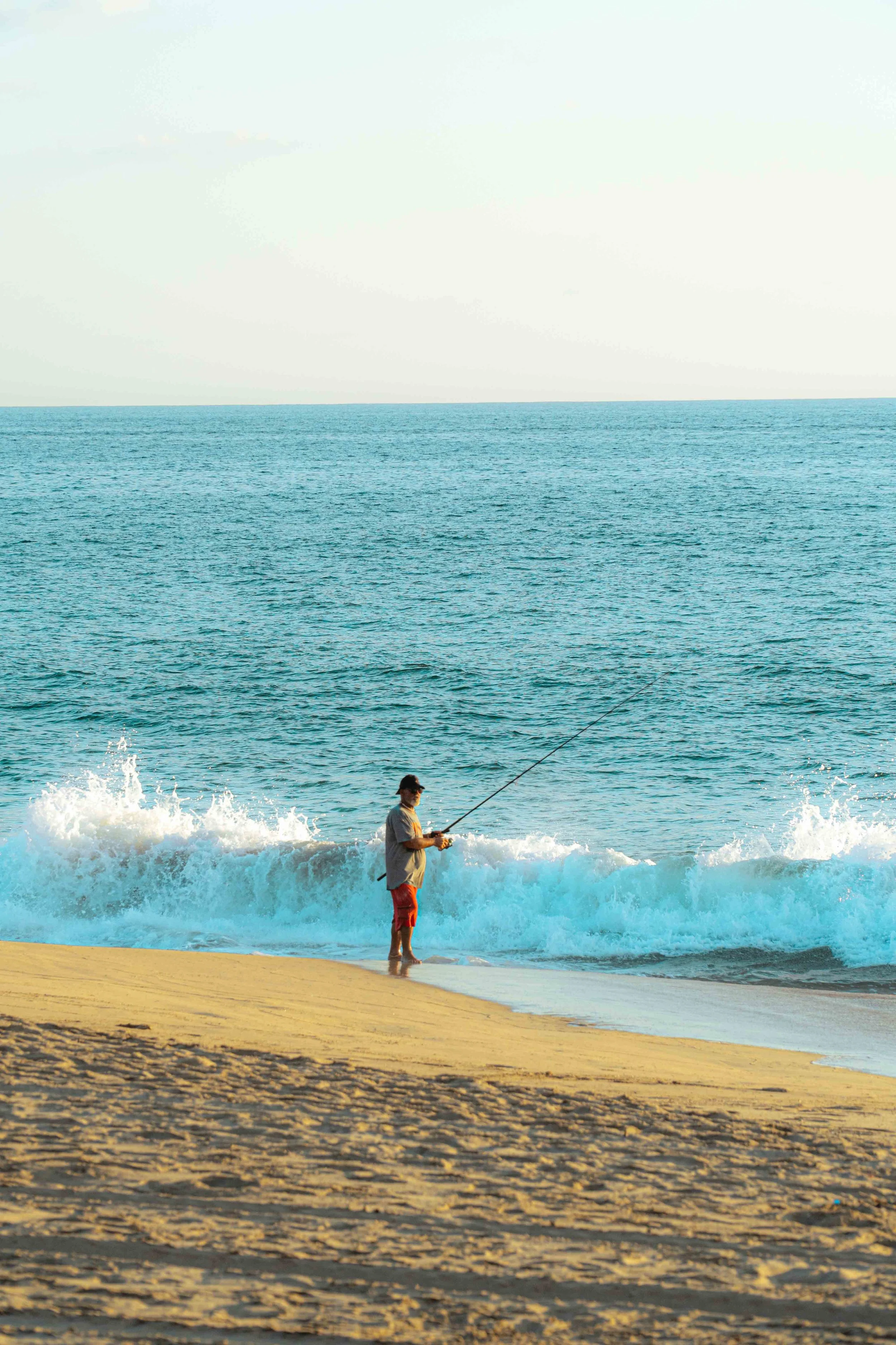 Persona pescando en la playa al atardecer con olas del mar y arena. hotel baxar pie de la cuesta 