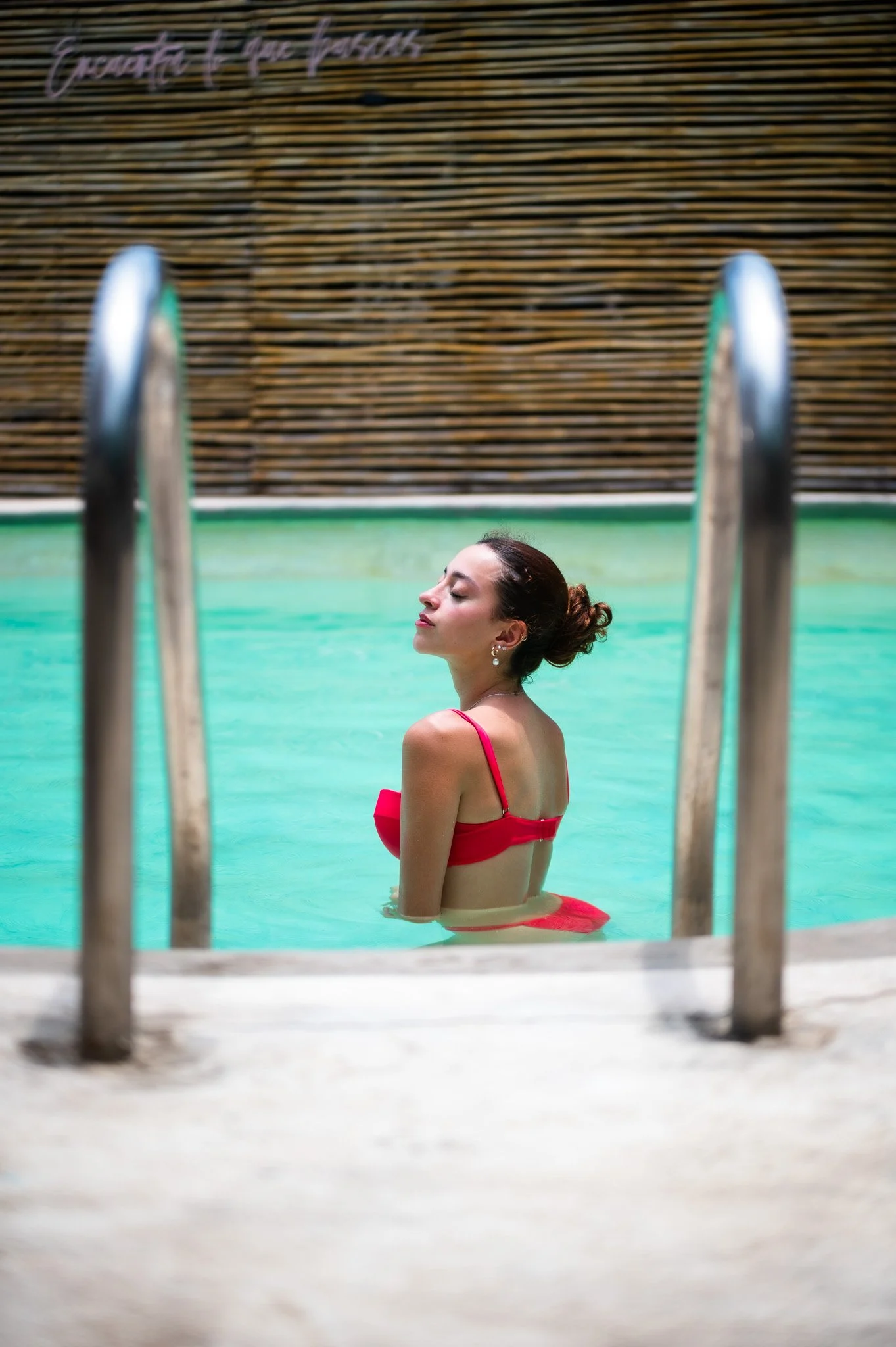 Mujer con vestido rojo en una alberca, vista lateral, con estructura de madera y letras en la pared que dicen 'encuentra lo que buscas'.  Hotel boutique baXar playa Pie de la cuesta Acapulco