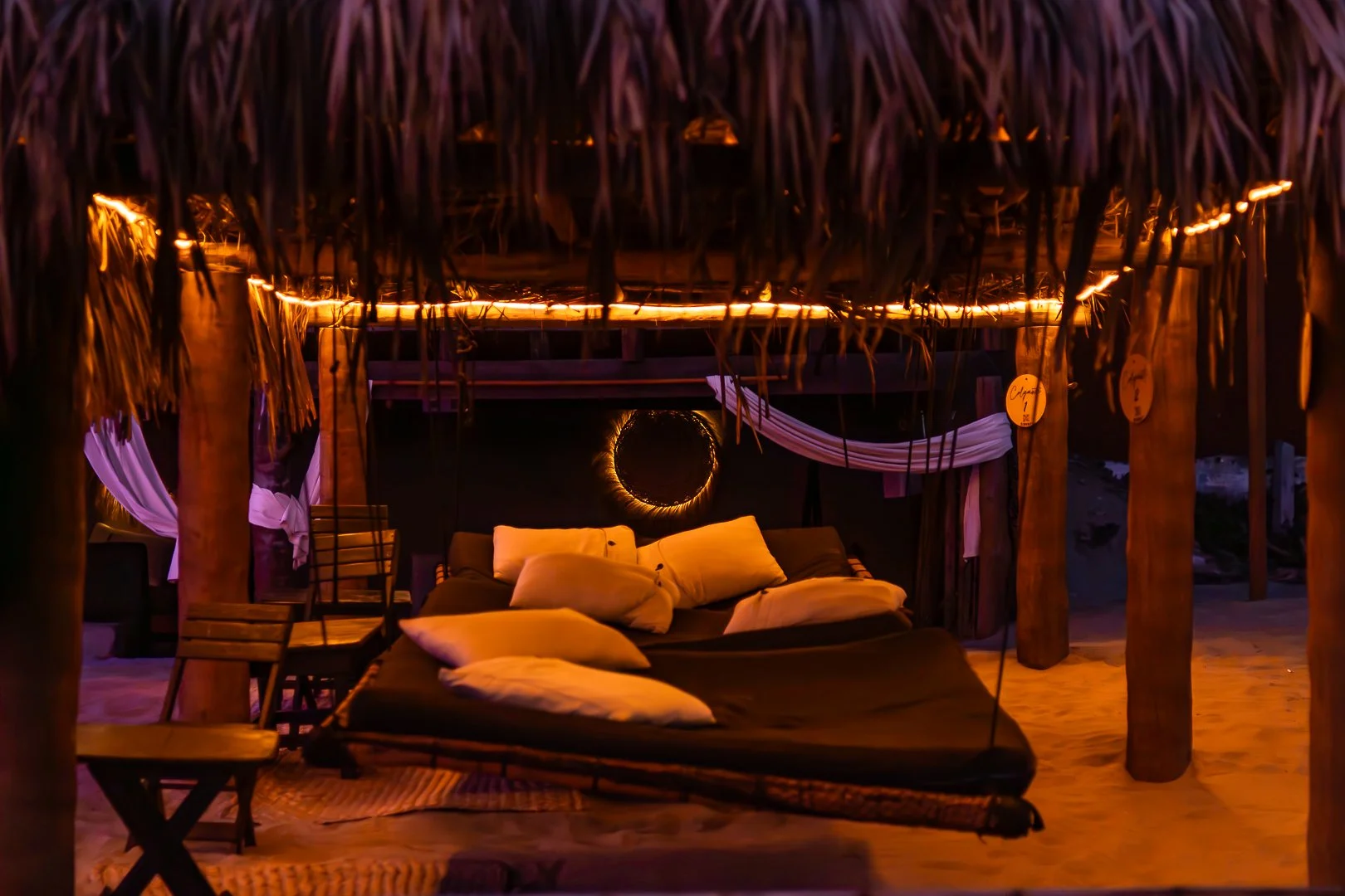 Terraza de playa con luces cálidas, camas colgantes con cojines, decorada con bambú y cortinas blancas. Hotel boutique playa pie de la cuesta, baXar Acapulco