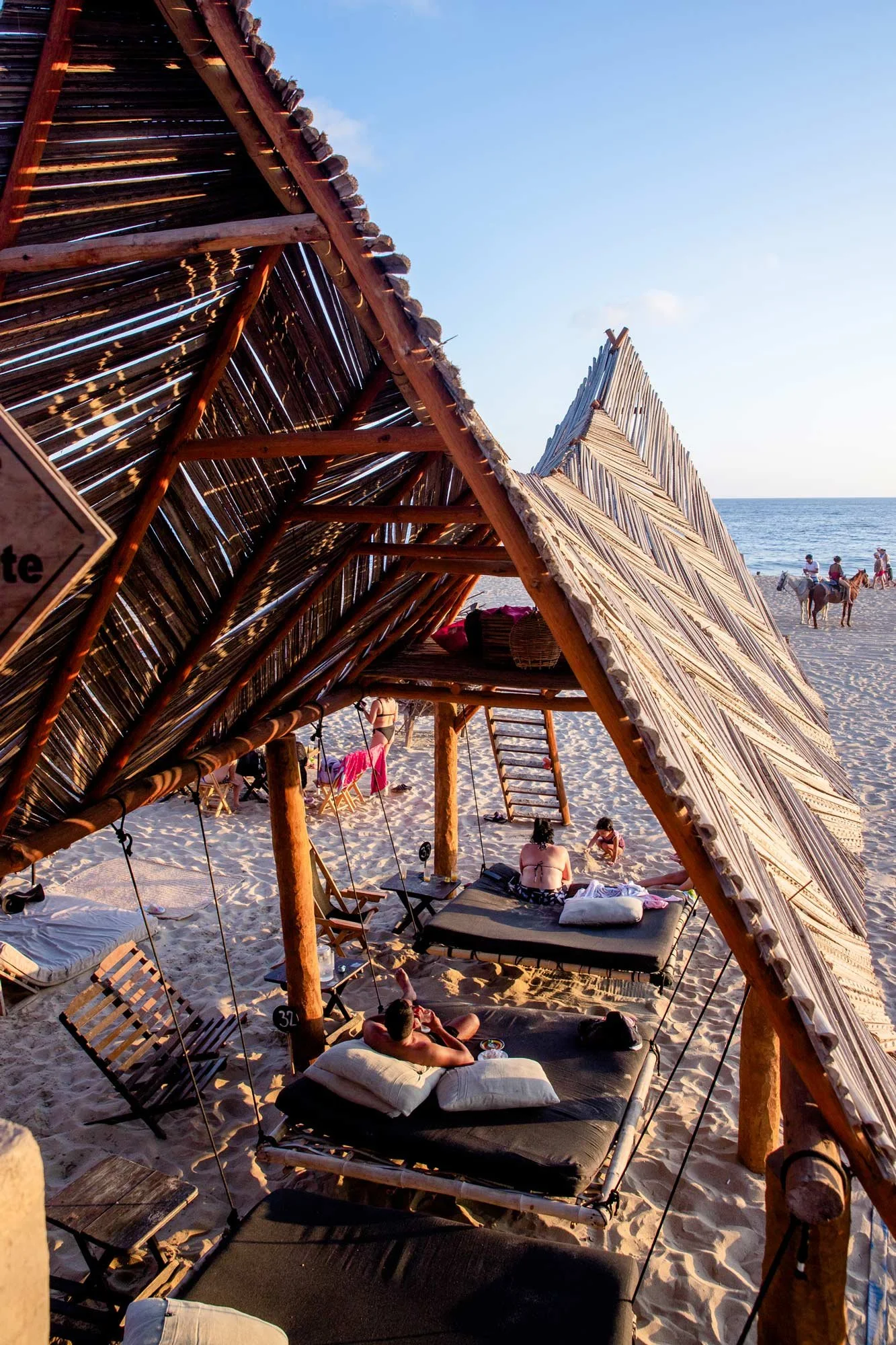 Chiringuitos de madera en la playa, con personas descansando y paseando cerca del mar, en un día soleado y despejado. hotel baXar club de playa pie de la cuesta acapulco guerrero