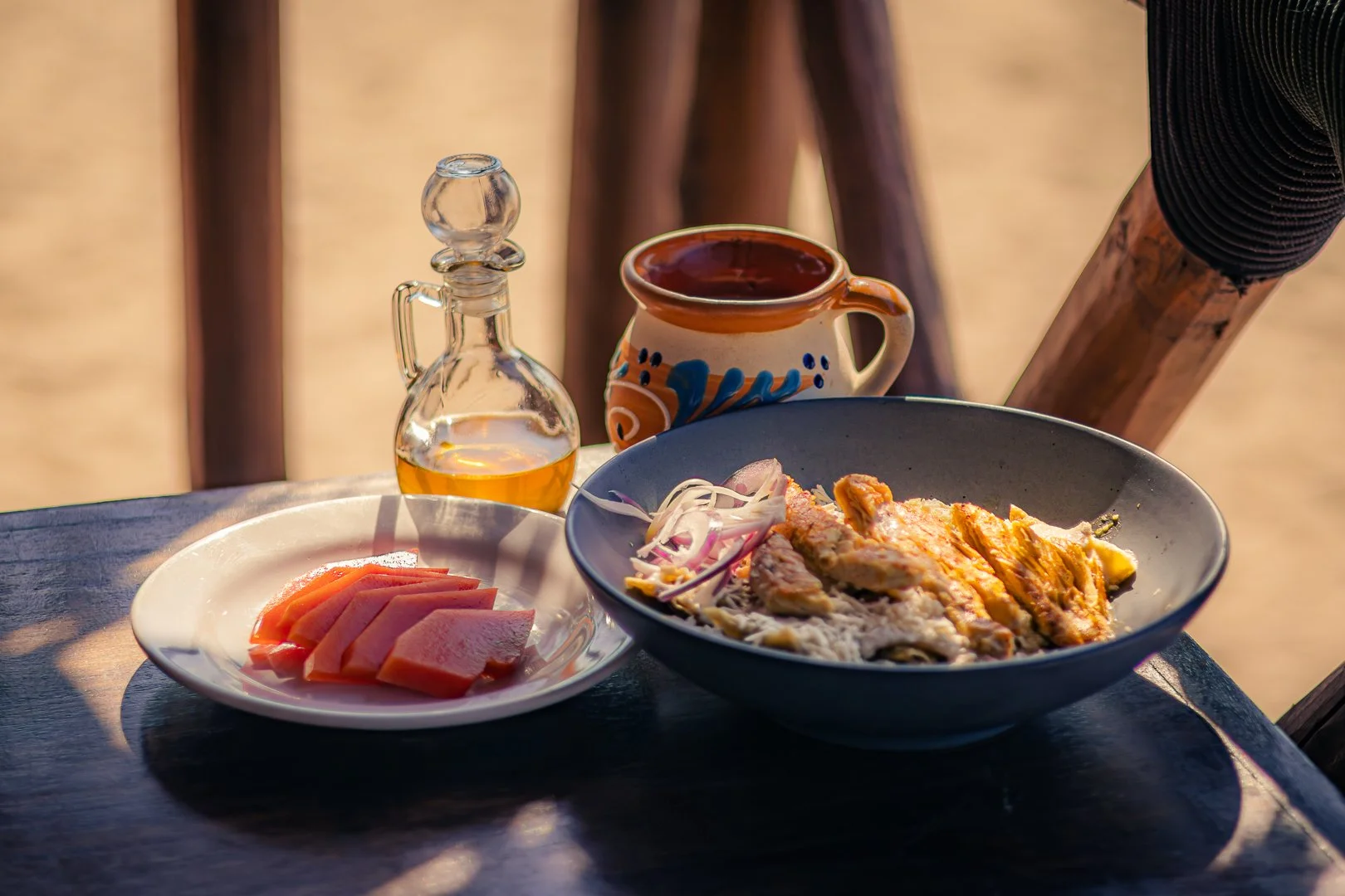 Comida tradicional mexicana en una mesa de madera, con plato de ceviche, una botella de tequila, una taza de barro con bebida, y papas con ajo y cebolla.  club de playa pie de la cuesta, hotel restaurante bar baXar acapulco