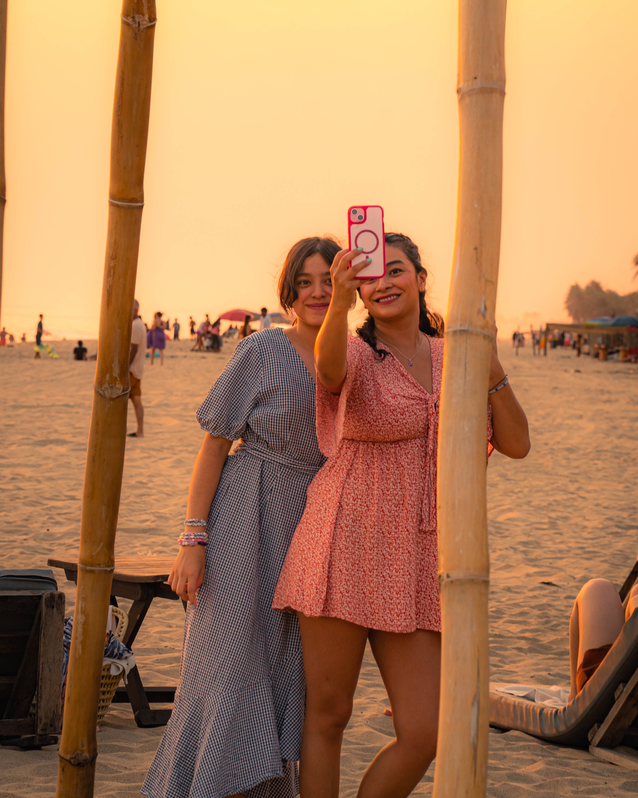 Dos mujeres toman una selfie en la playa al atardecer en playa pie de la cuesta, instalación de  bambú como marco en primer plano.  Hotel boutique baXar playa Pie de la cuesta Acapulco