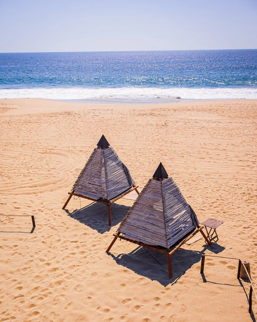 Dos cabañas de palapa en la playa con mar y cielo despejado al fondo.  Hotel boutique baXar club de playa Pie de la cuesta Acapulco. Beach Club 