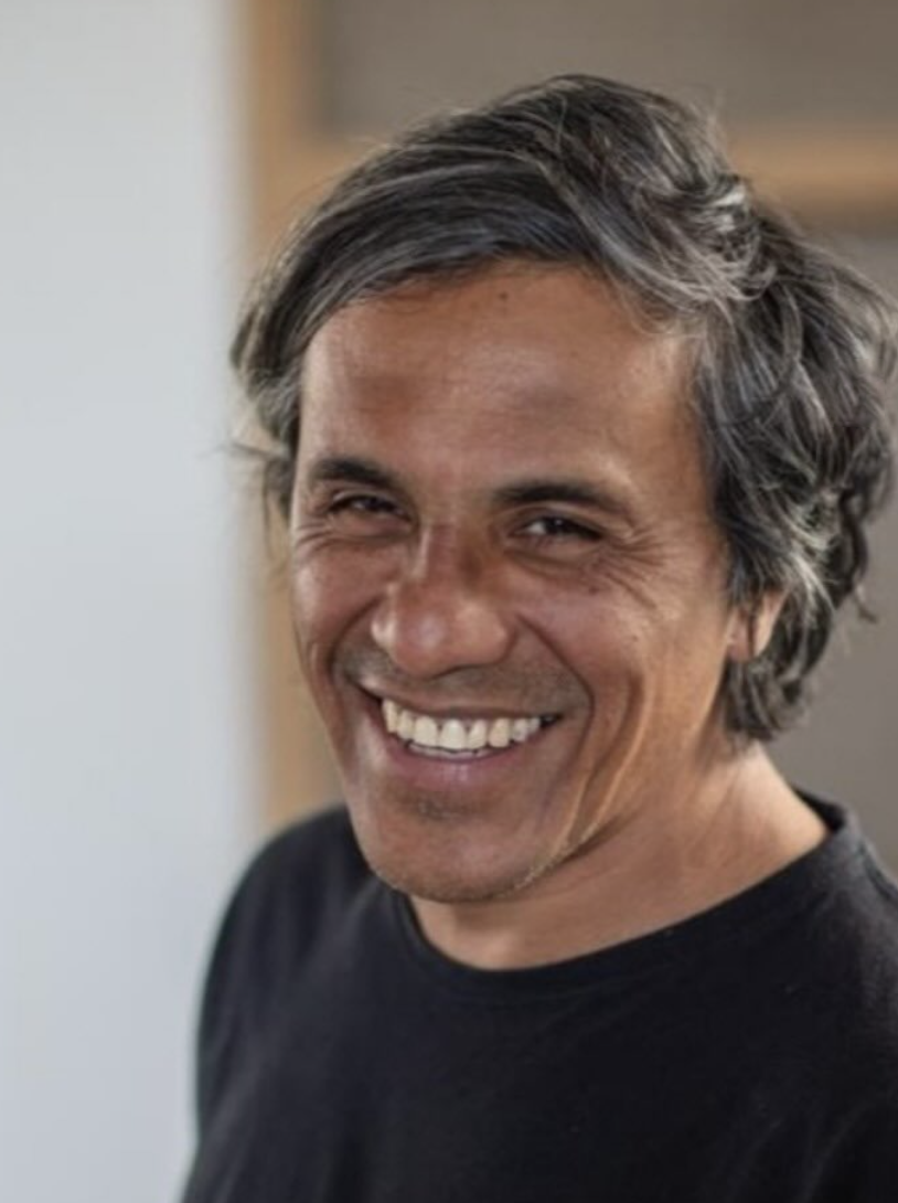 Hombre con cabello gris y sonrisa amplia, vestido con camiseta negra