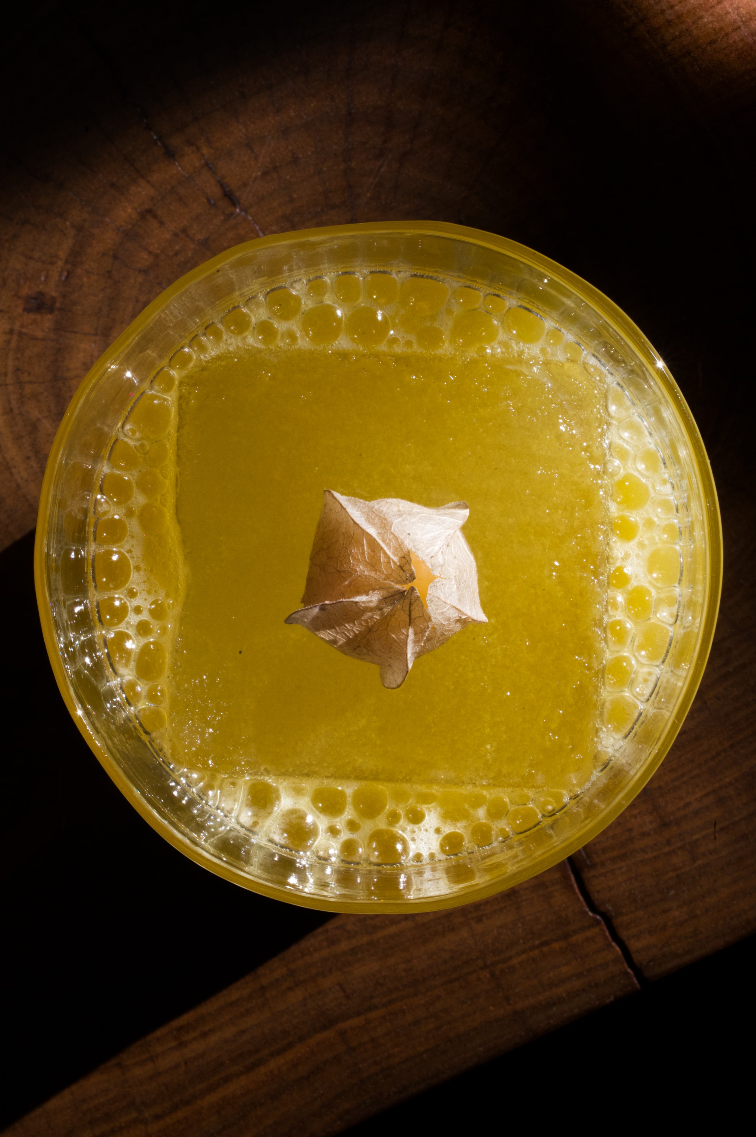 Cocktail avec une crisallide flottant dessus, posé sur une table en bois.