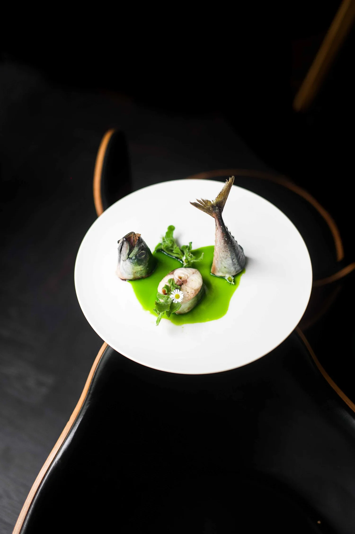 Assiette de poisson avec sauce verte, garnie de fleurs et d'herbes, présentée sur une assiette blanche