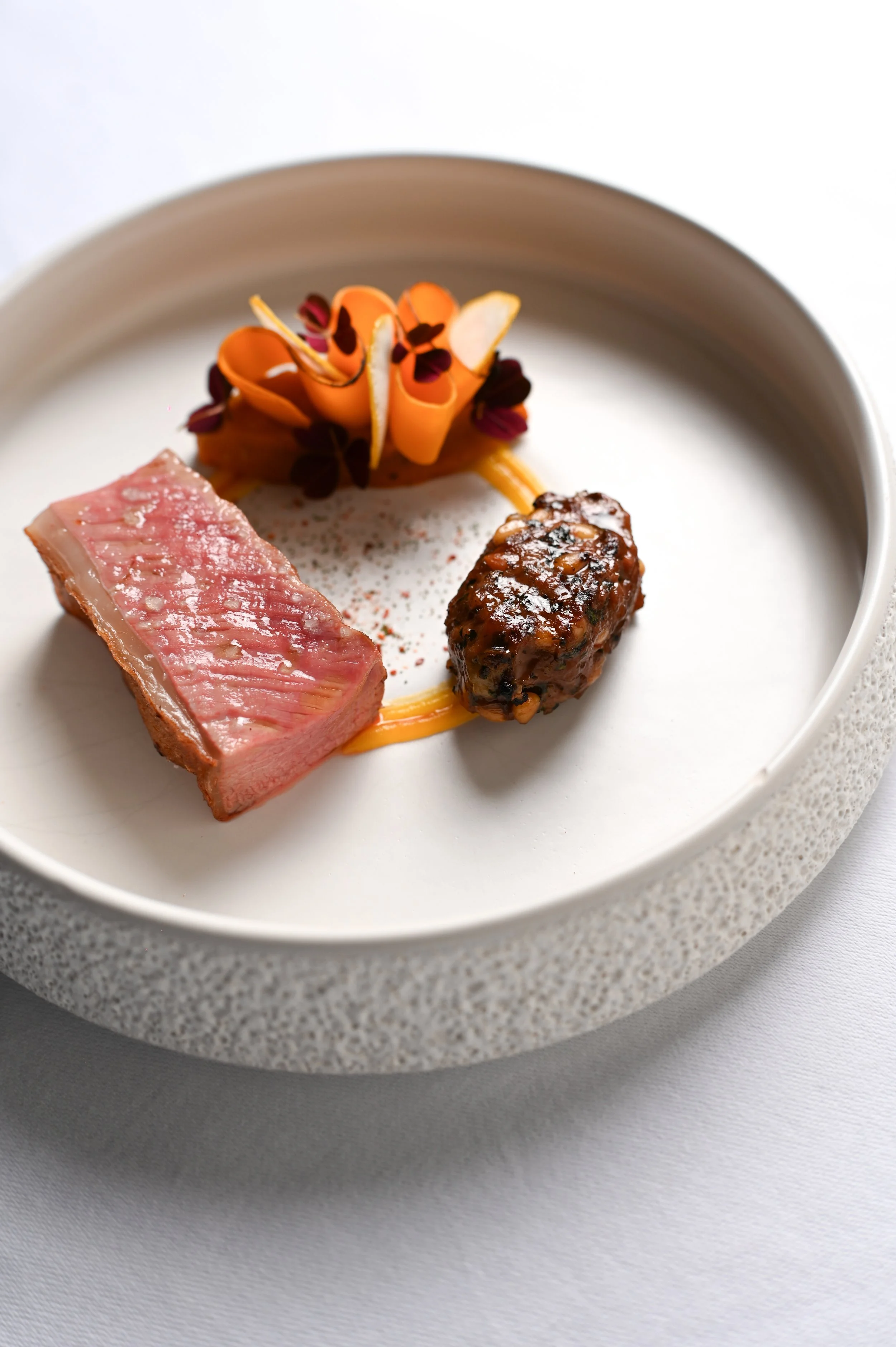 Assiette gastronomique avec trois morceaux de viande, décoration végétale et sauce