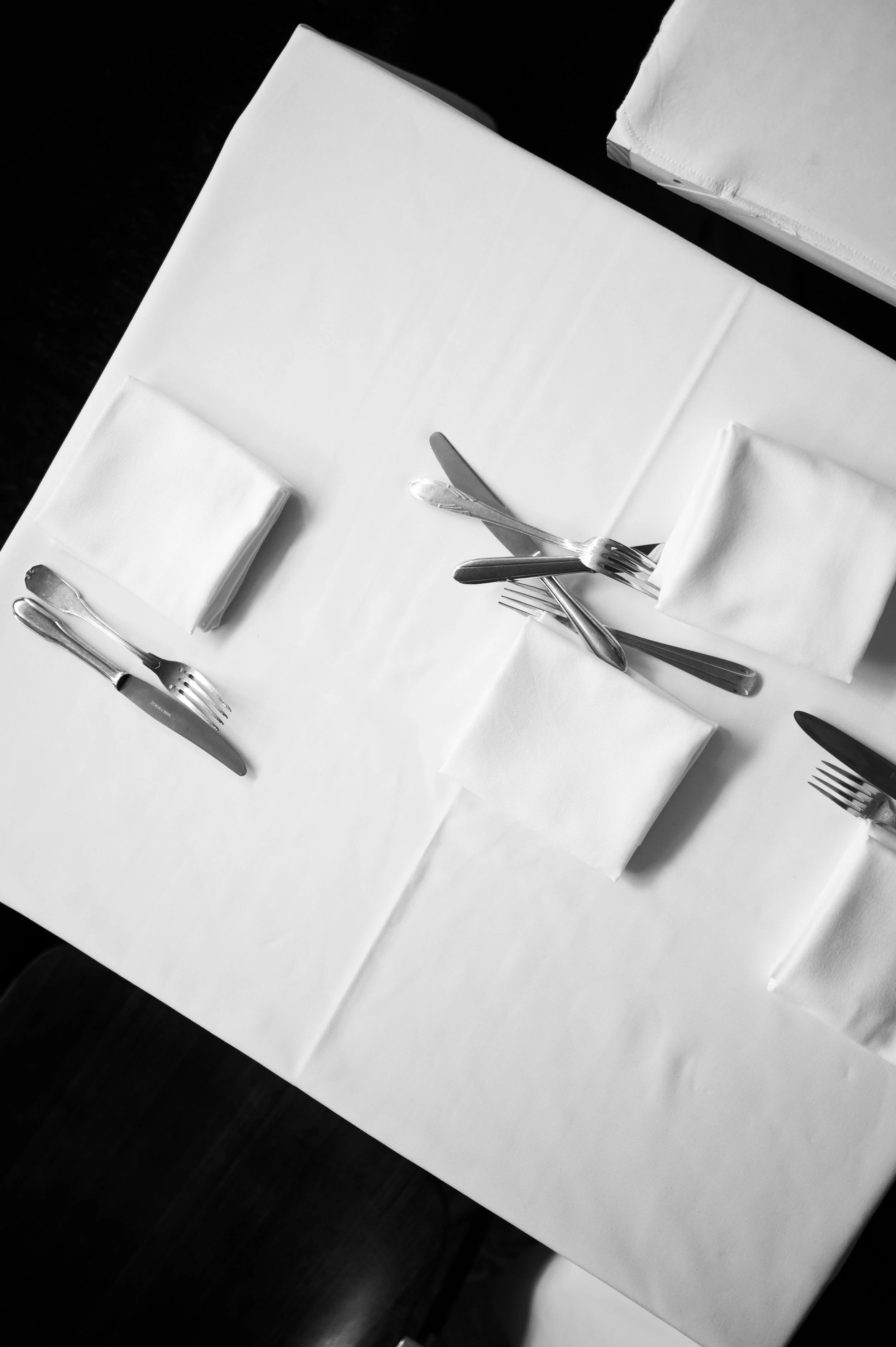 Tables de restaurant avec assiettes, couverts, serviettes en papier, sur une nappe blanche, vue en plongée.