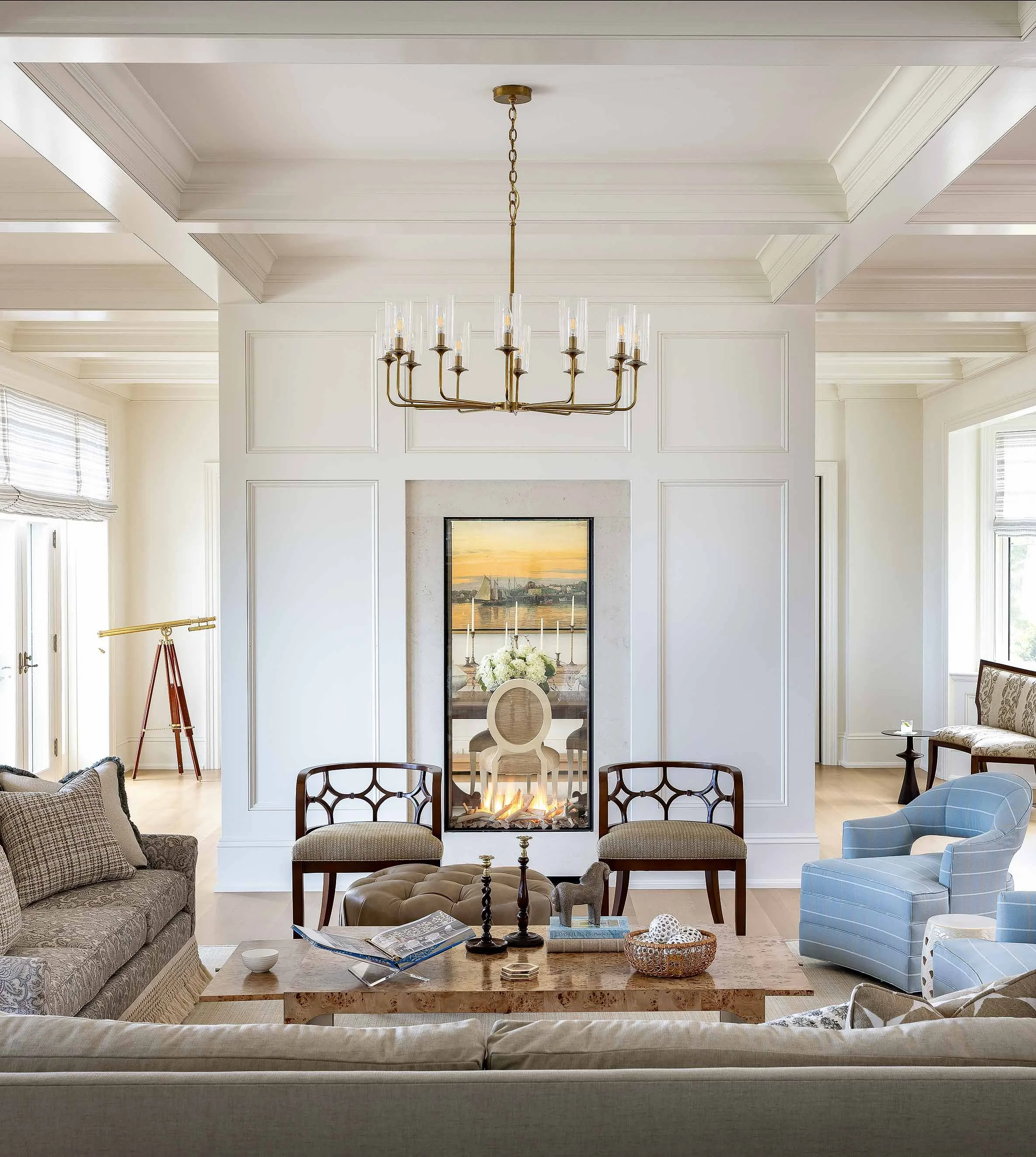 Living room with a flat-screen TV showing an American football game, above a modern fireplace, with a glass coffee table, a sofa, and armchairs in a well-lit space.