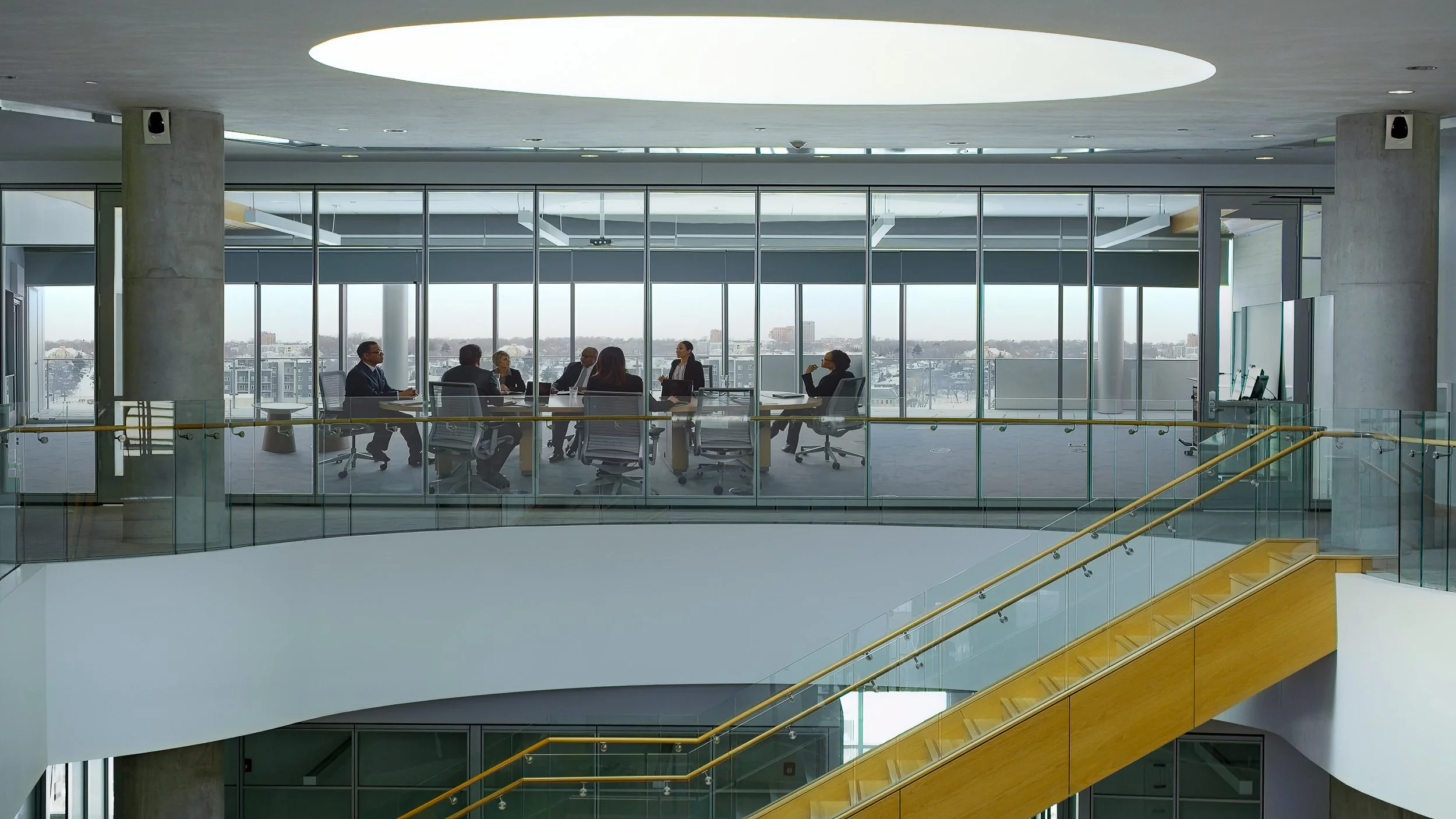 Businesspeople in a modern office conference room with glass walls and large windows, overlooking a cityscape, engaged in a meeting.