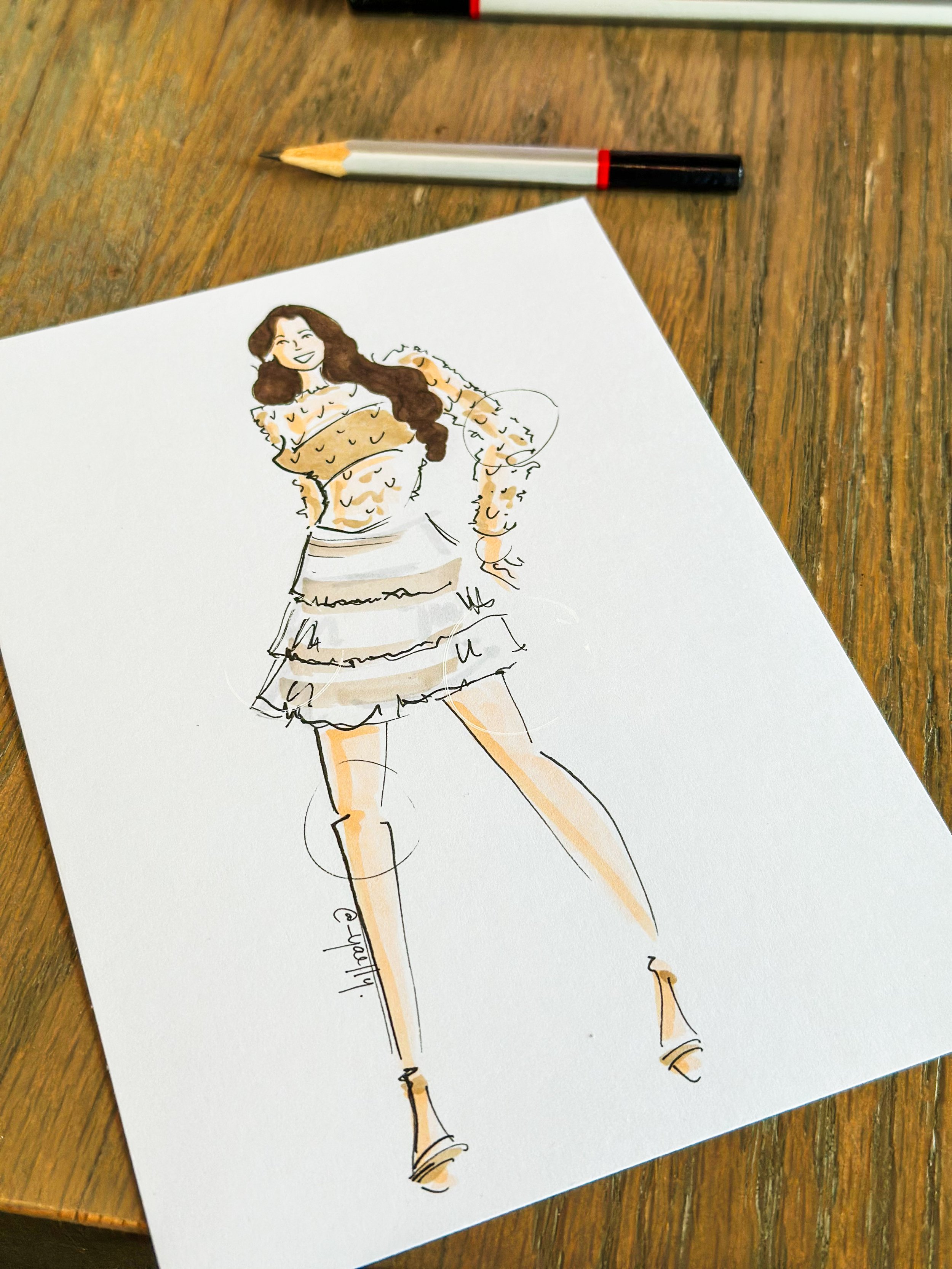 Fashion illustration of a woman with long dark hair wearing a striped skirt, fur jacket, and tall boots, on a white sheet of paper on a wooden table, with a pencil nearby.