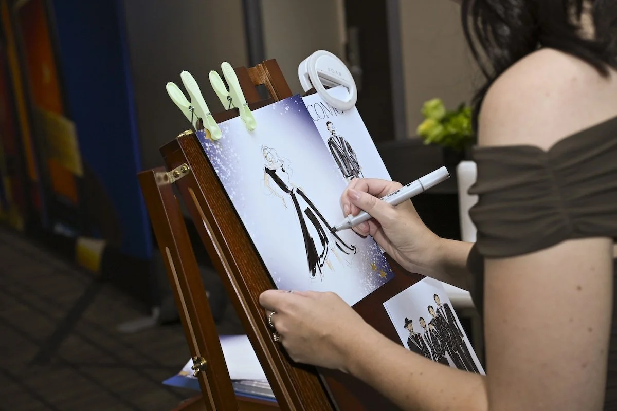 An artist drawing a fashion illustration on a drawing board with photos of fashion models attached.