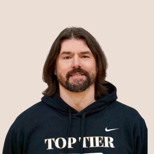 A man with shoulder-length brown hair and a beard wearing a black hoodie with the Nike logo and the words 'TOP TIER' printed on it, standing against a white background.