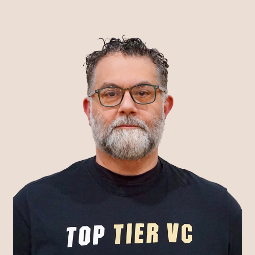 A middle-aged man with gray hair and beard wearing glasses and a black T-shirt that says 'TOP TIER VC' in white and gold letters.