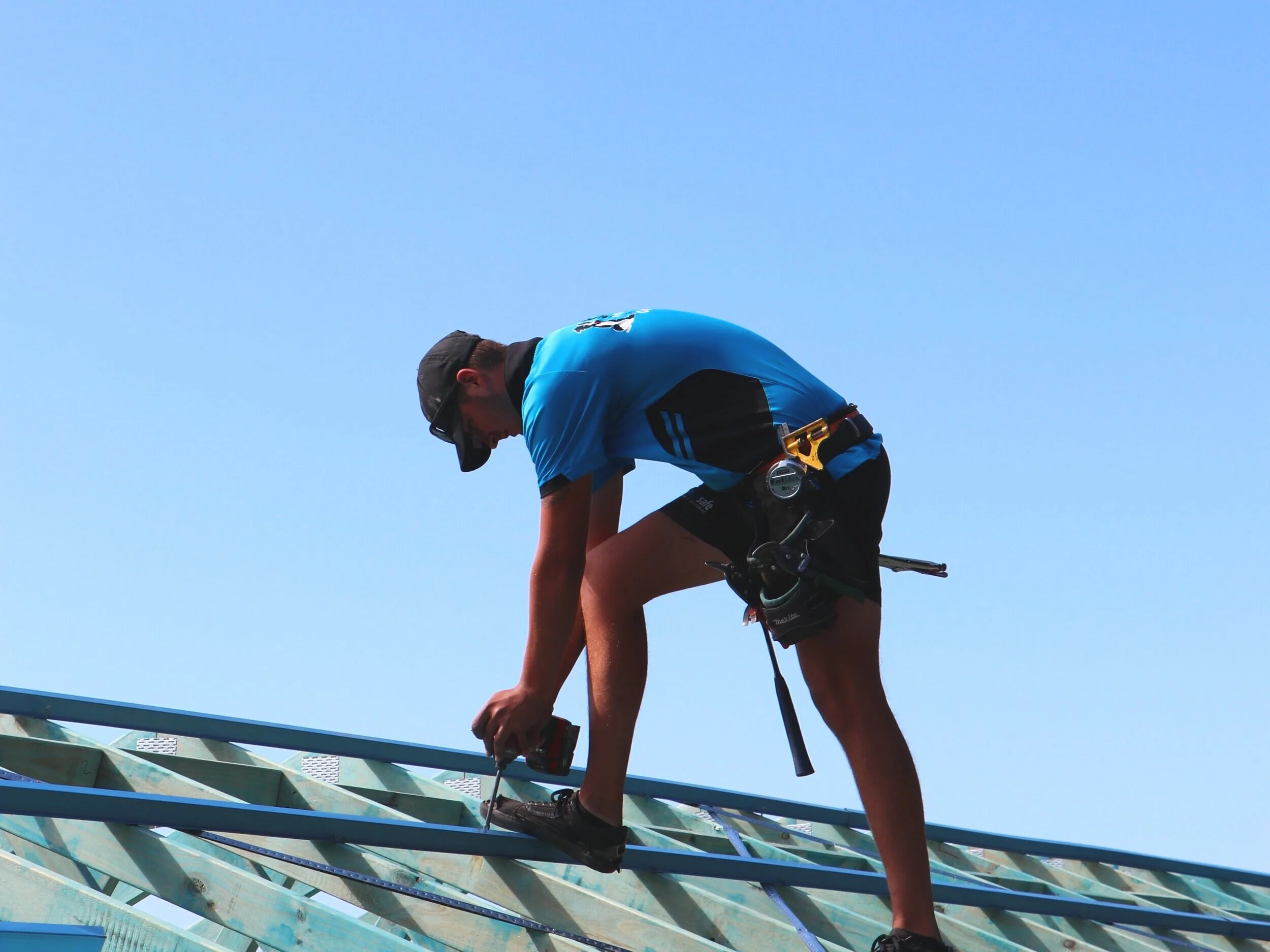 A construction worker wearing safety glasses, a yellow high-visibility jacket, and gloves, installing or repairing electrical wiring or conduit in a building.