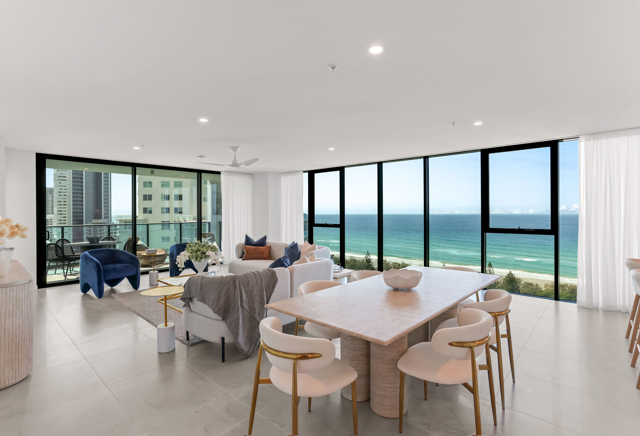 Large living room with couch and kitchen tale and floor to ceiling windows   