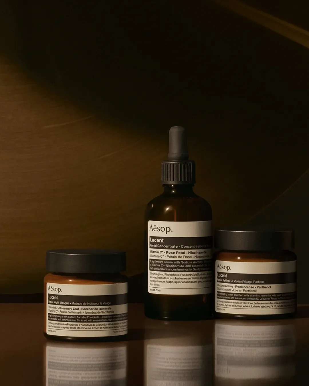 A dark, moody arrangement of amber glass Aesop skincare jars and a dropper bottle.