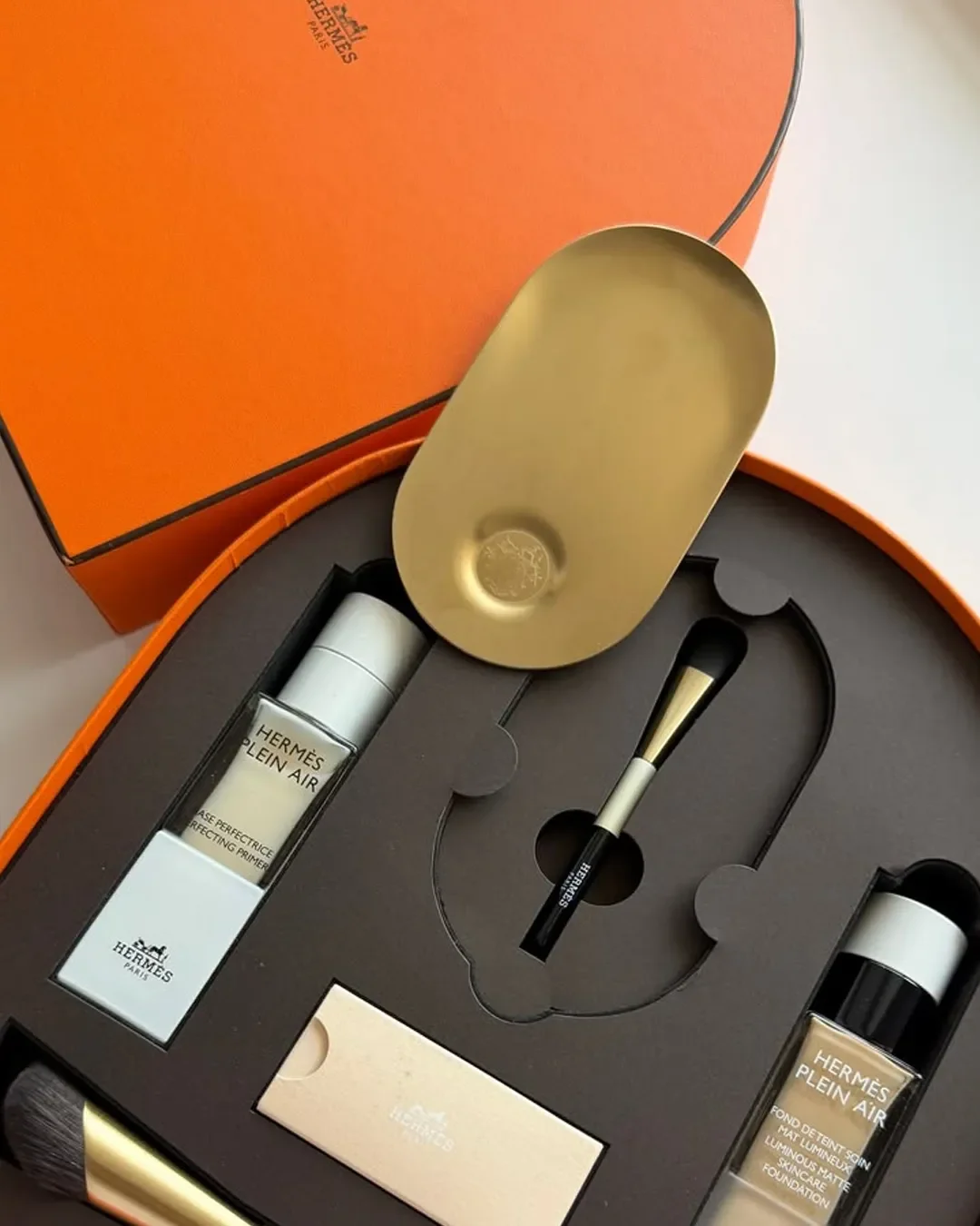 Hermes beauty packaging, gift box containing high-end cosmetics, brushes, and a gold metal tray.