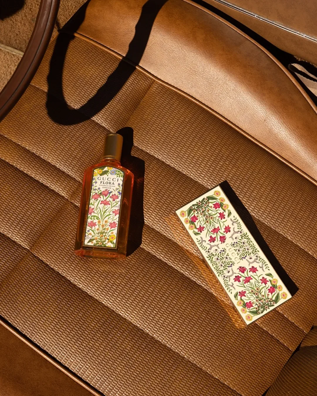 A Gucci Flora perfume bottle and its floral illustrated box laying on a vintage leather car seat.