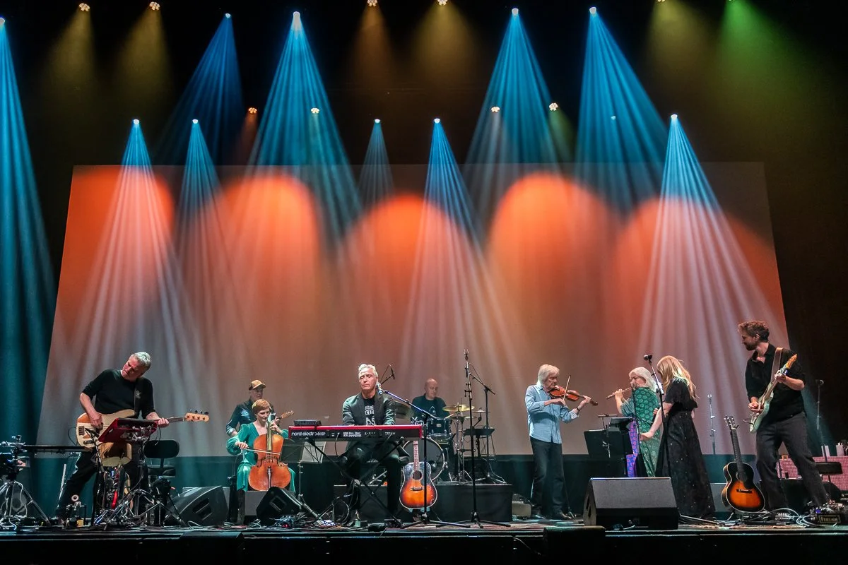 En musikgruppe spiller på scenen med farverige lys, herunder blå, orange og gule spotlights.