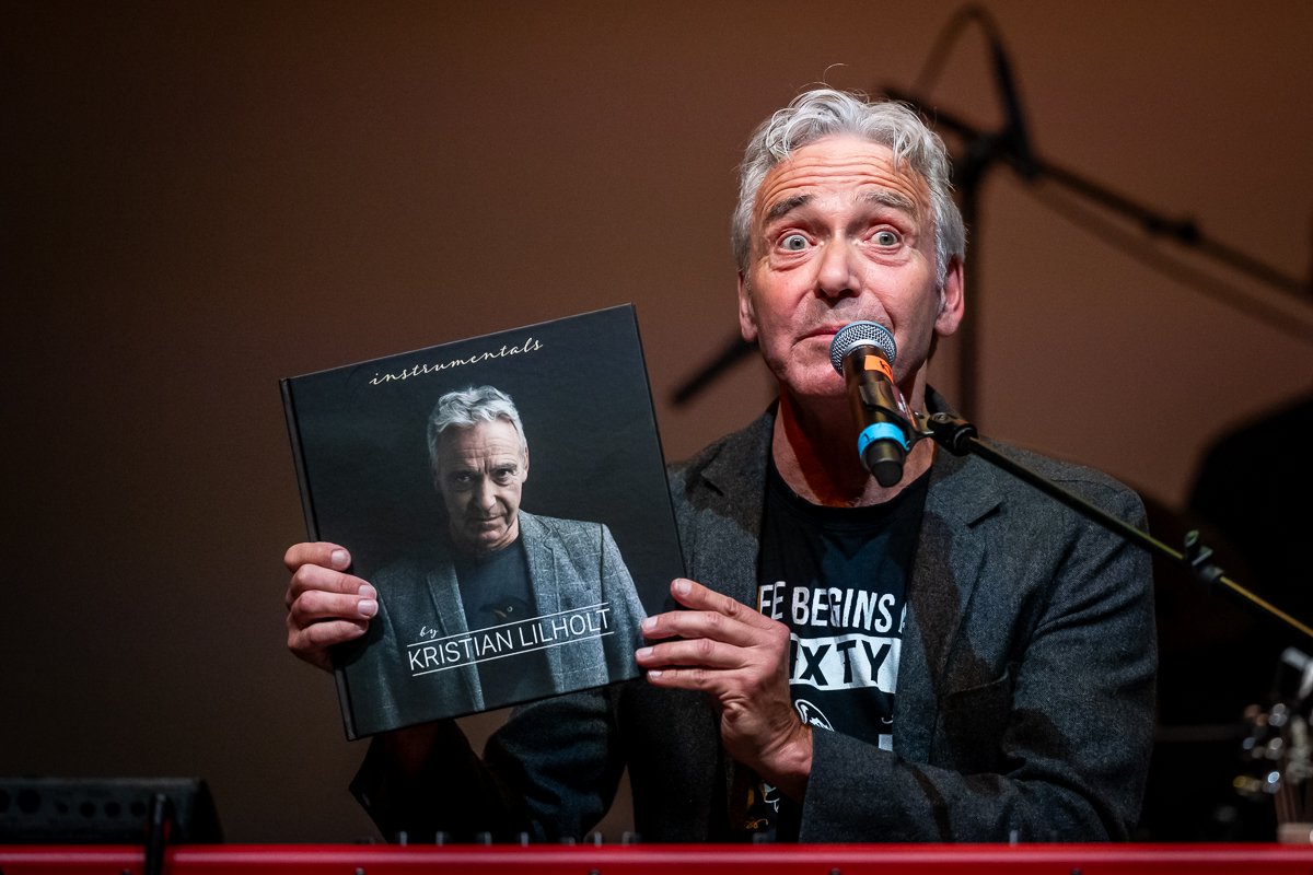 En mand med gråt hår holder en vinylplade med albumcoveret 'instrumentals' af Kristian Lilholt, mens han taler i mikrofon.