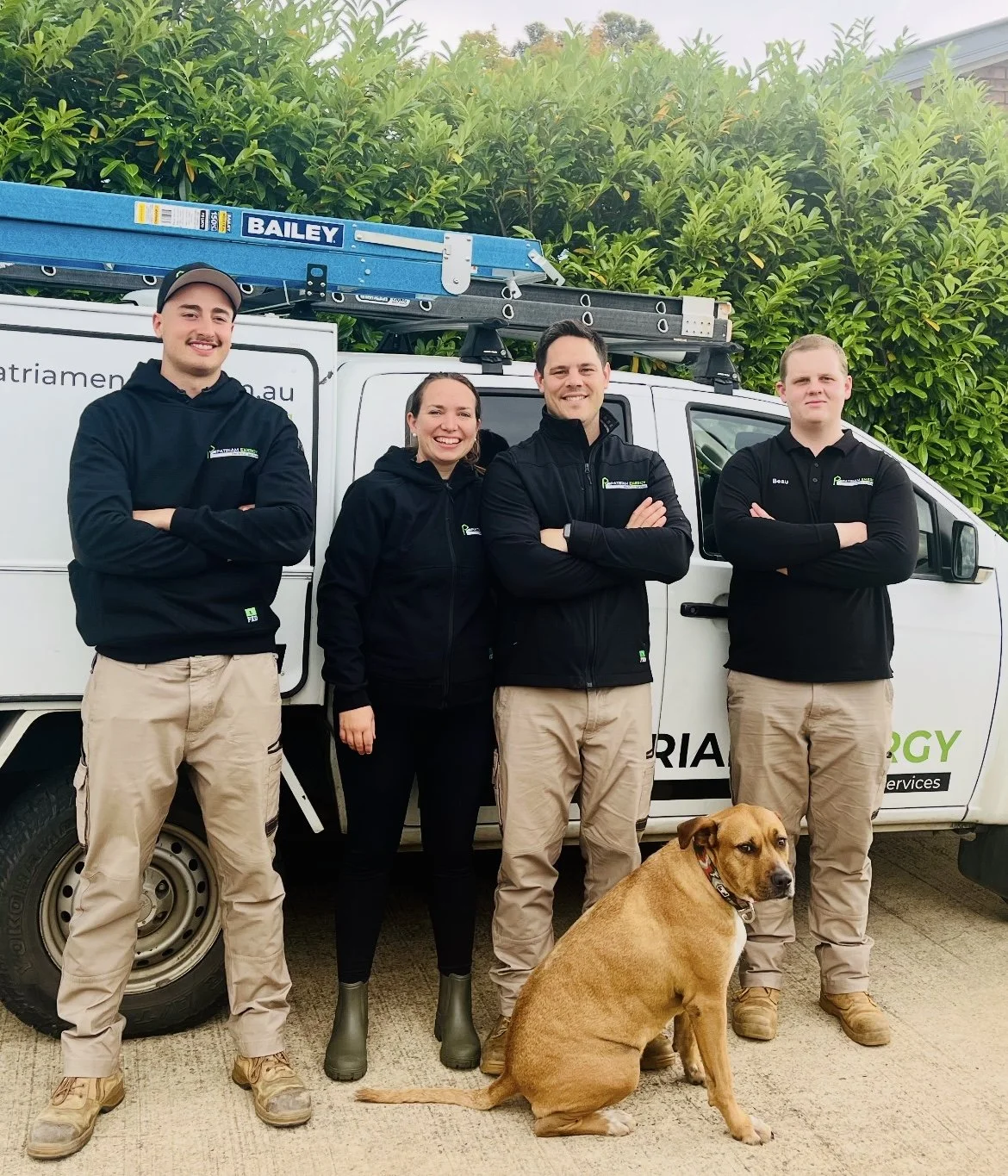 Four workers and a dog standing in front of a company van with tools on the roof.