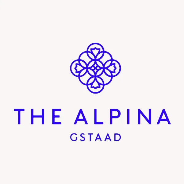 Logo mit blauer, stilisierte Schneeflocke und Text "THE ALPINA GSTAAD" auf weißem Hintergrund.