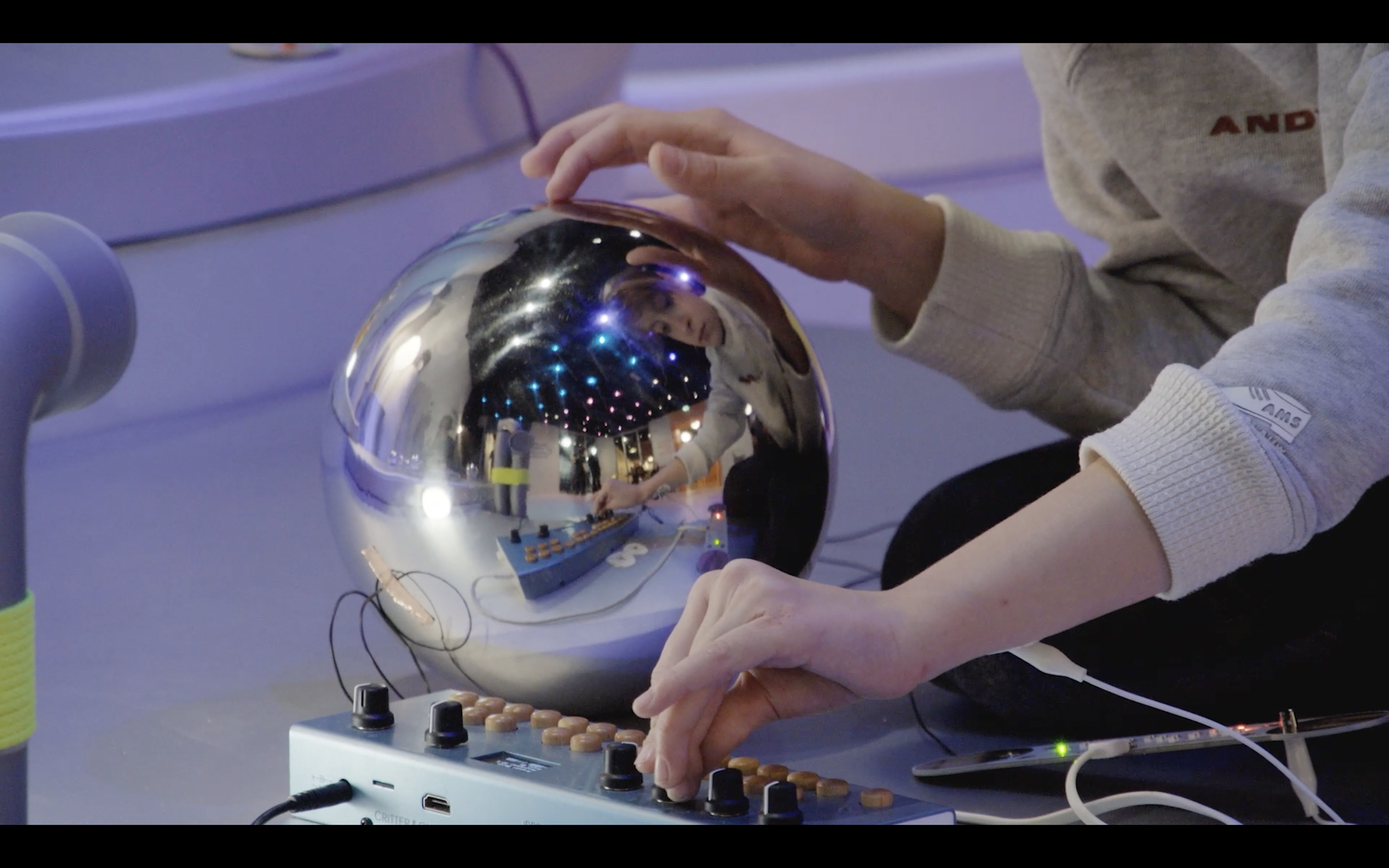 Person interacting with a reflective, metallic sphere in an indoor setting with purple lighting.