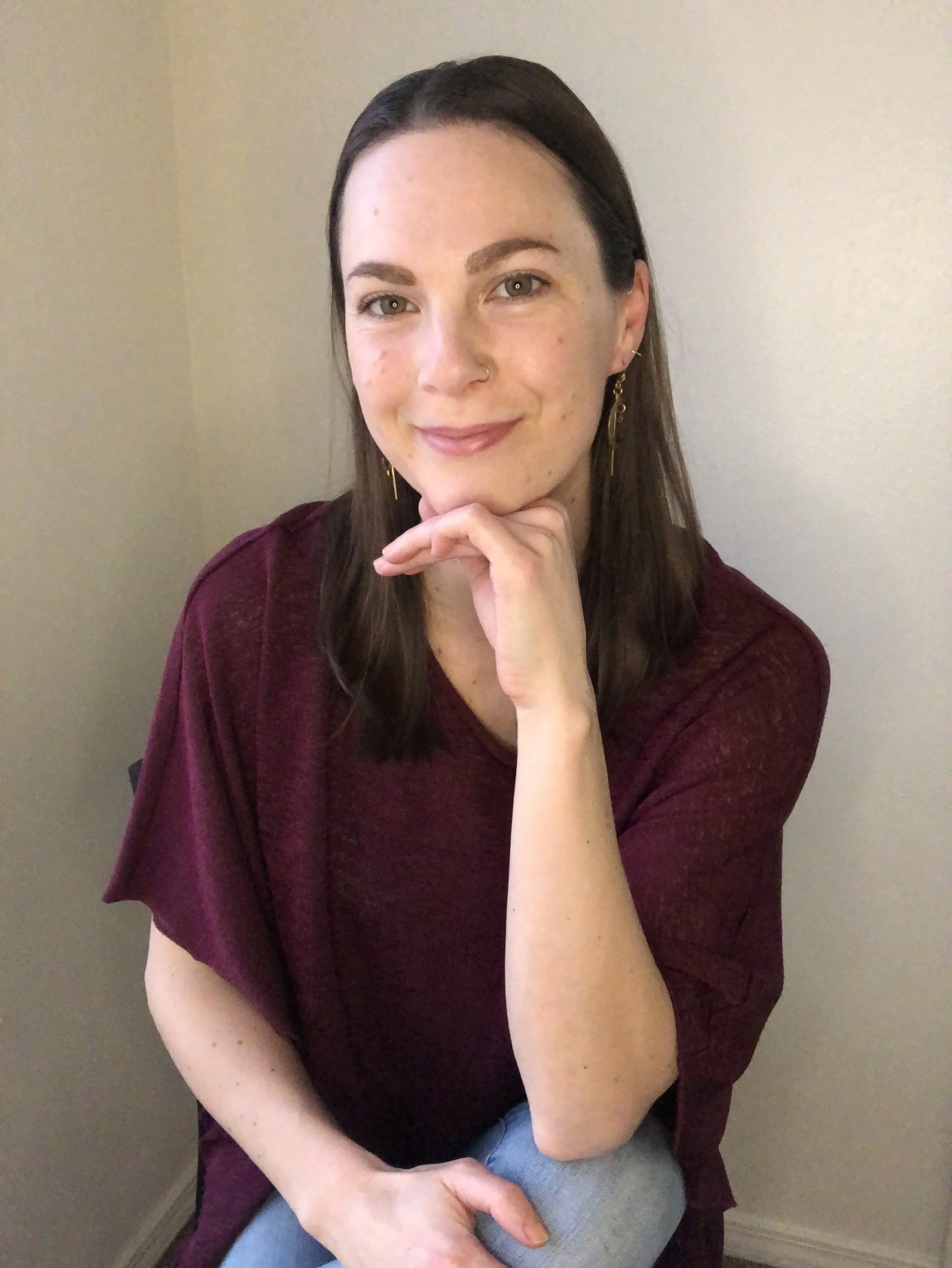woman in professional maroon top smiling with her chin rested on her hand