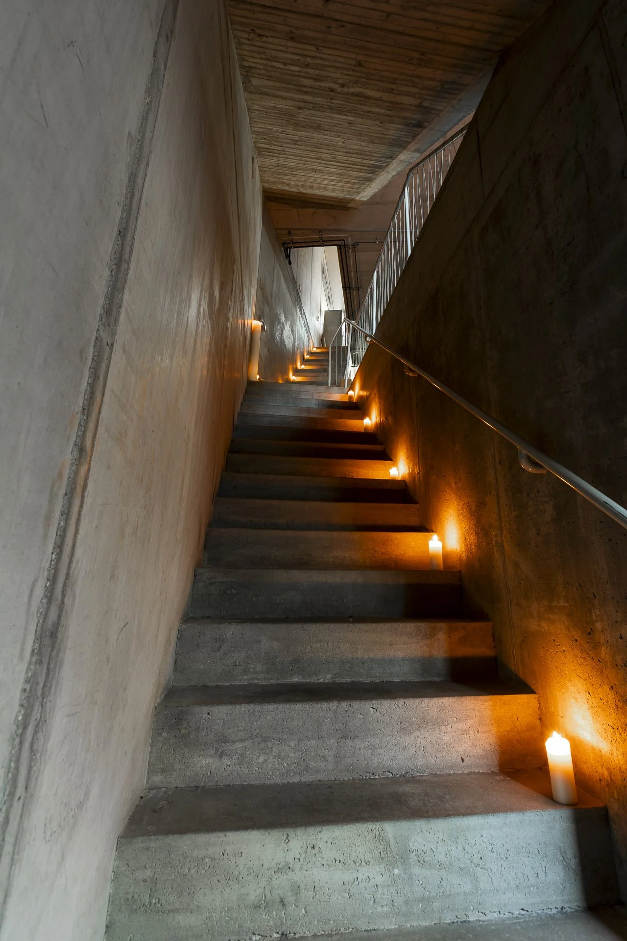 Concrete staircase with candles on each step, leading upwards alongside a concrete wall, in a dimly lit indoor setting.